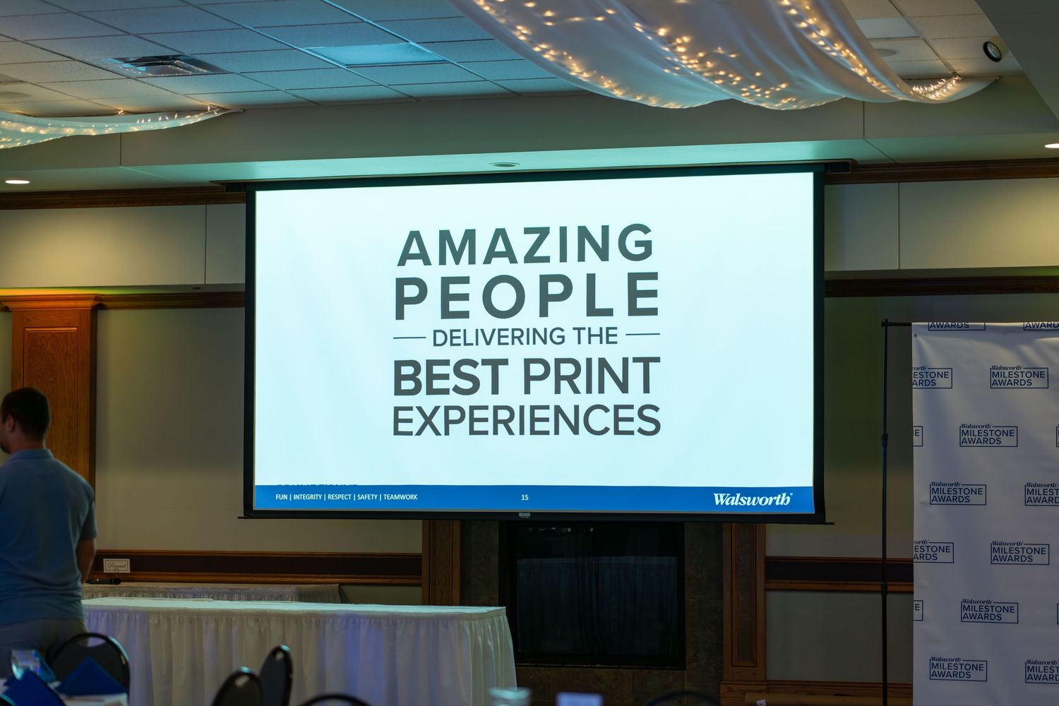 A large projection screen displays text reading 'AMAZING PEOPLE BEST PRINT EXPERIENCES' in a conference room setting.