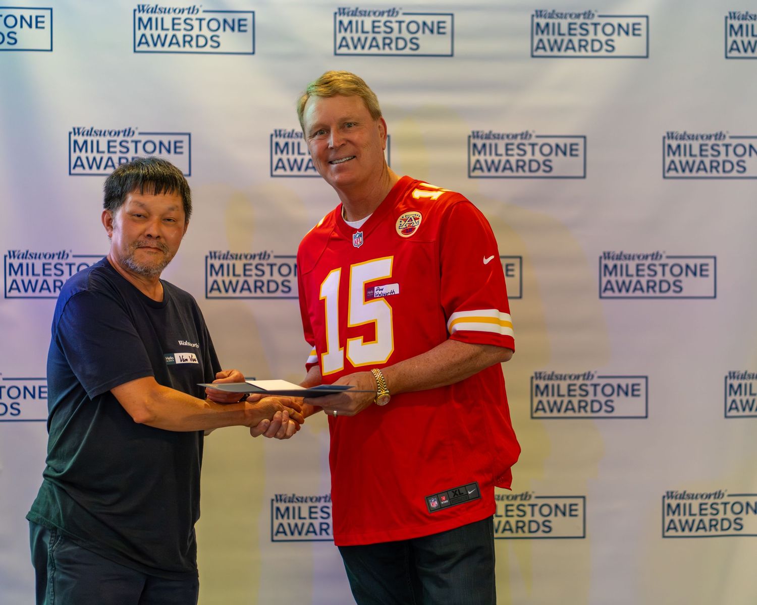 A row of people in red and dark shirts shake hands while standing against a backdrop with Milestone Awards text.