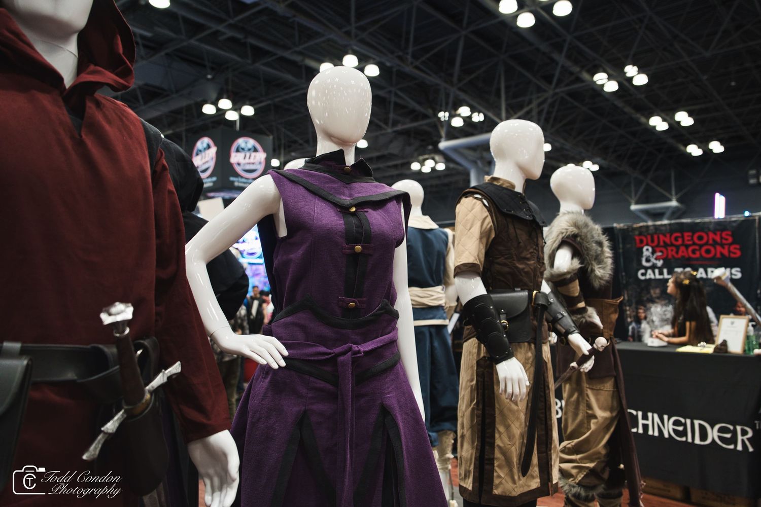 Mannequins displaying elaborate fantasy costumes at a convention booth with Dungeons and Dragons signage in the background.