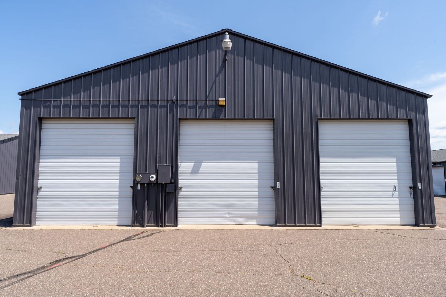Row of black metal storage units with white roll-up doors on a concrete foundation in a commercial storage facility.