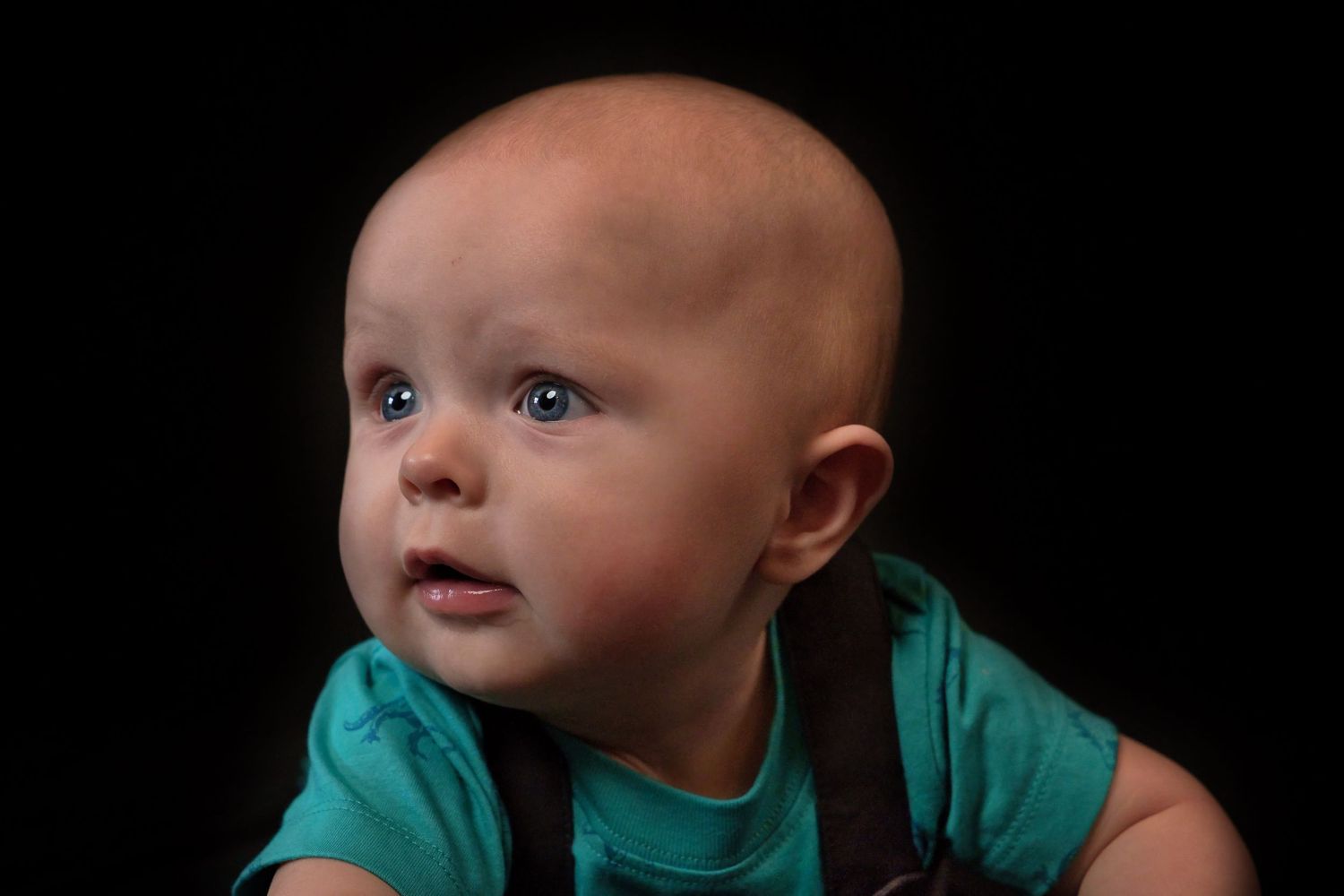 A baby in a teal shirt crawls and looks up with curiosity while exploring.