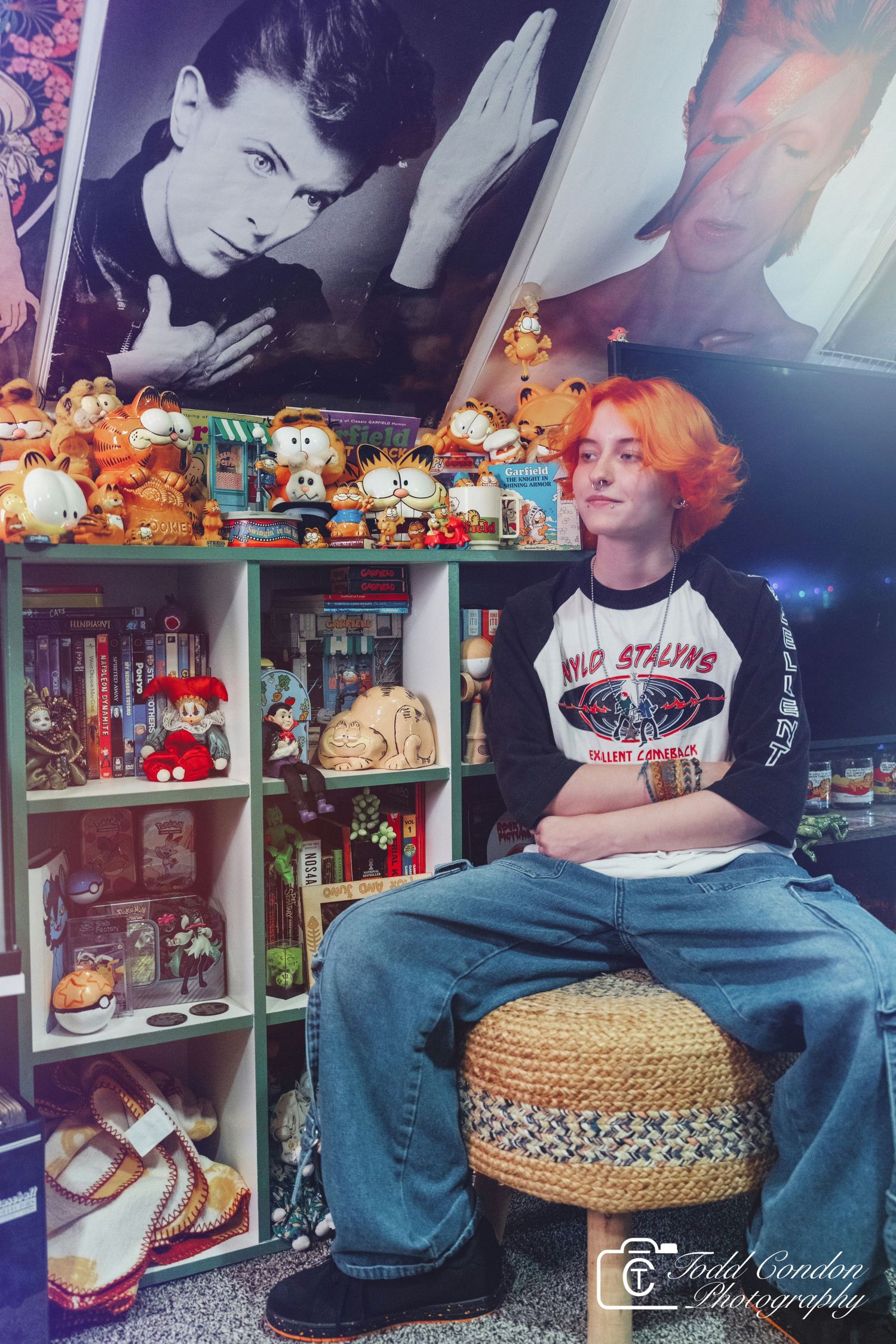 Collection of toy memorabilia displayed on shelves with someone sitting on a woven stool in a collector's room.