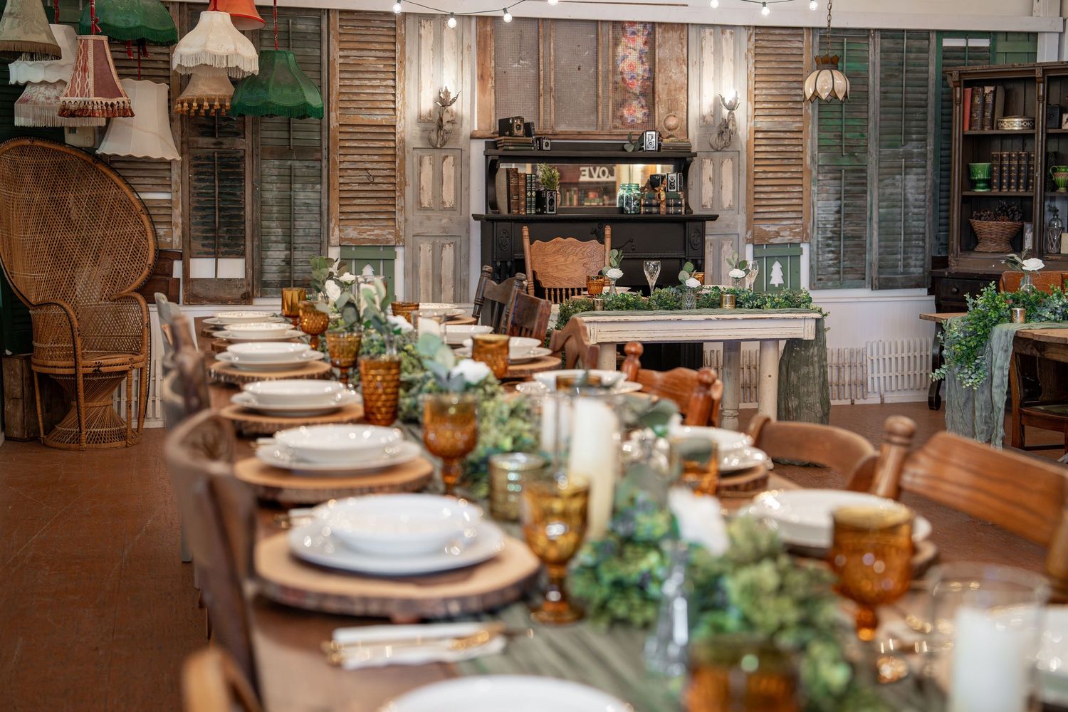 Rustic wooden dining table set with elegant place settings, greenery centerpieces and glowing pendant lights in restaurant.