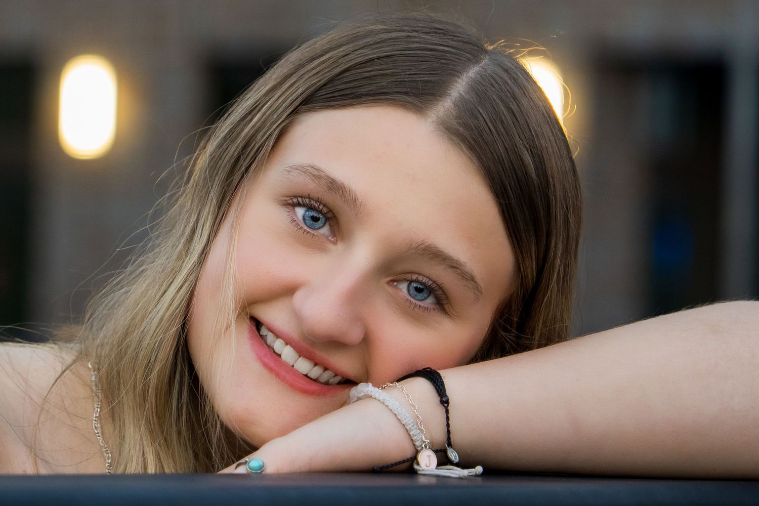 A person rests their head on their arms while smiling warmly at the camera in soft evening lighting.