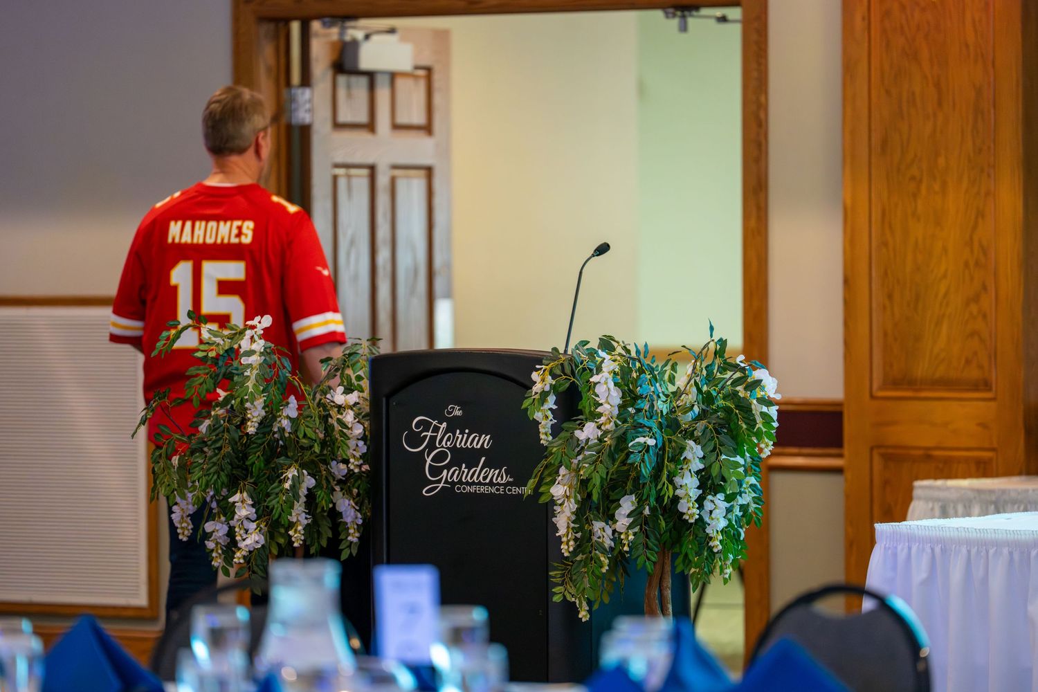 Red sports jerseys hang on display at a formal event with wooden paneling and decorative greenery.