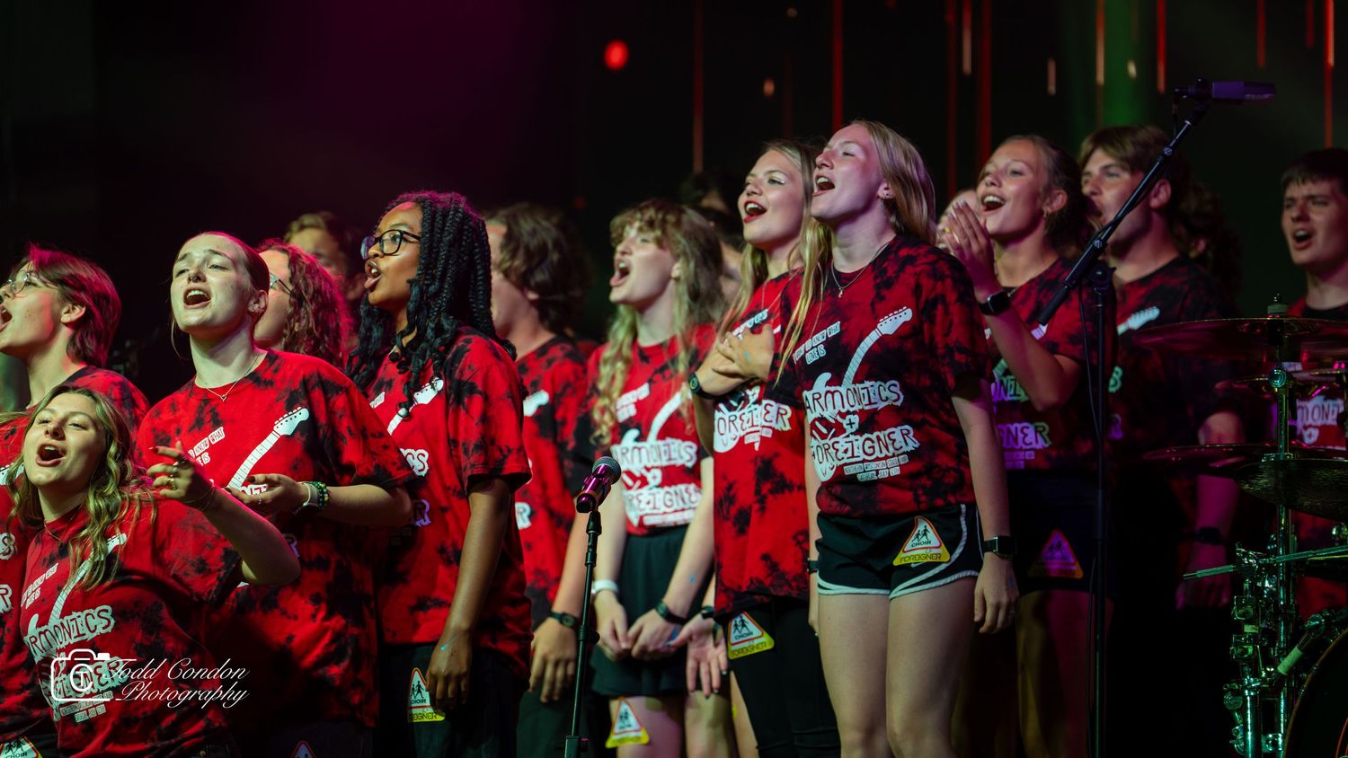 A panoramic view of performers in red uniforms standing in a row on stage during a musical performance.