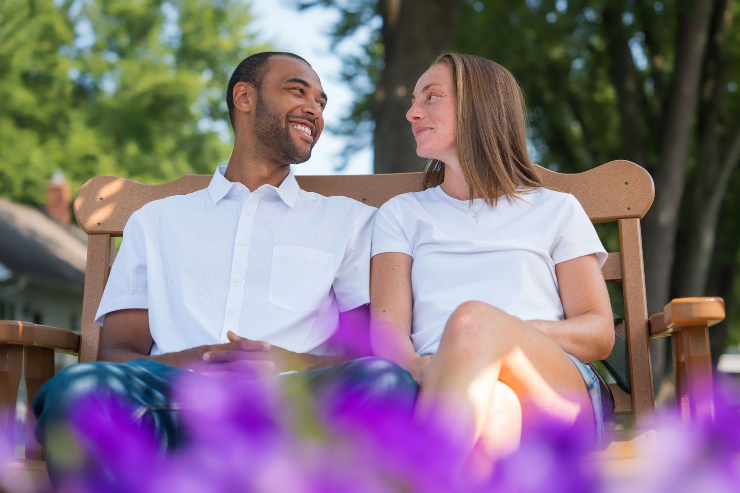 Couple sitting on wooden chairs in a garden with purple flowers in the foreground during golden hour.