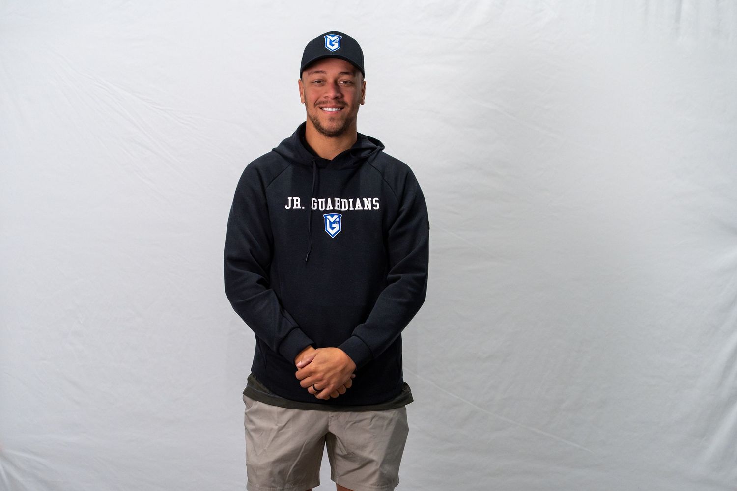 Professional wearing a black hoodie and khaki pants poses against a white backdrop in a studio setting.