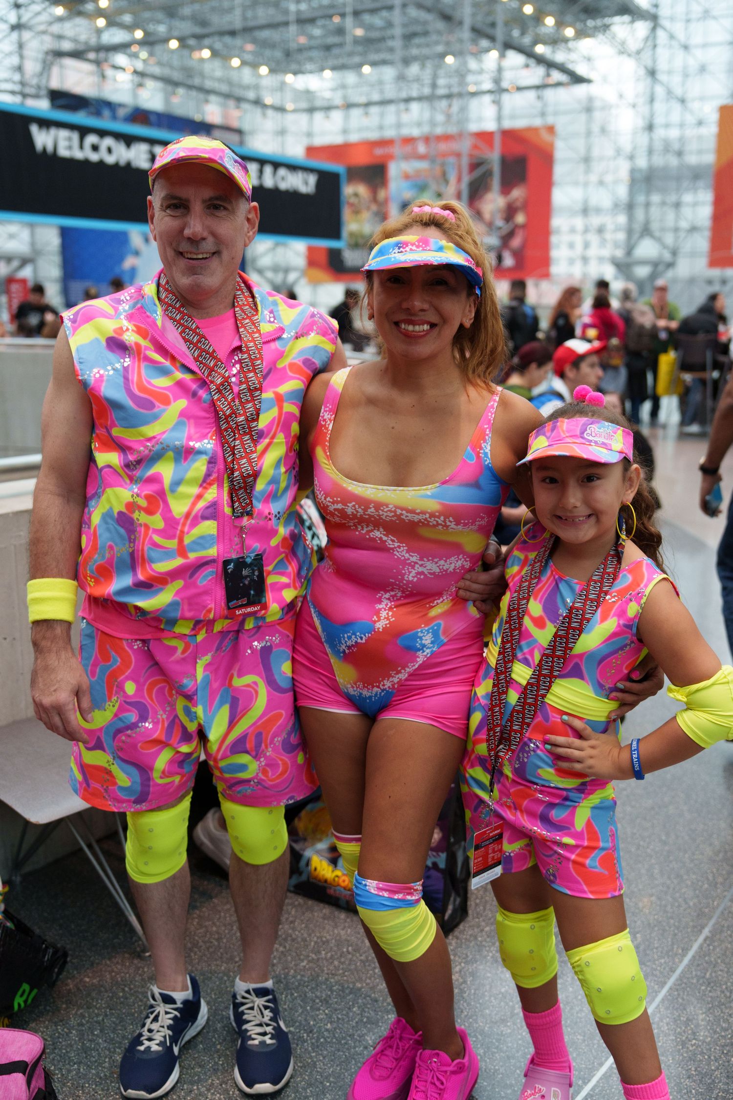 Family of three in matching neon 80s aerobic costumes posing at a convention center event.