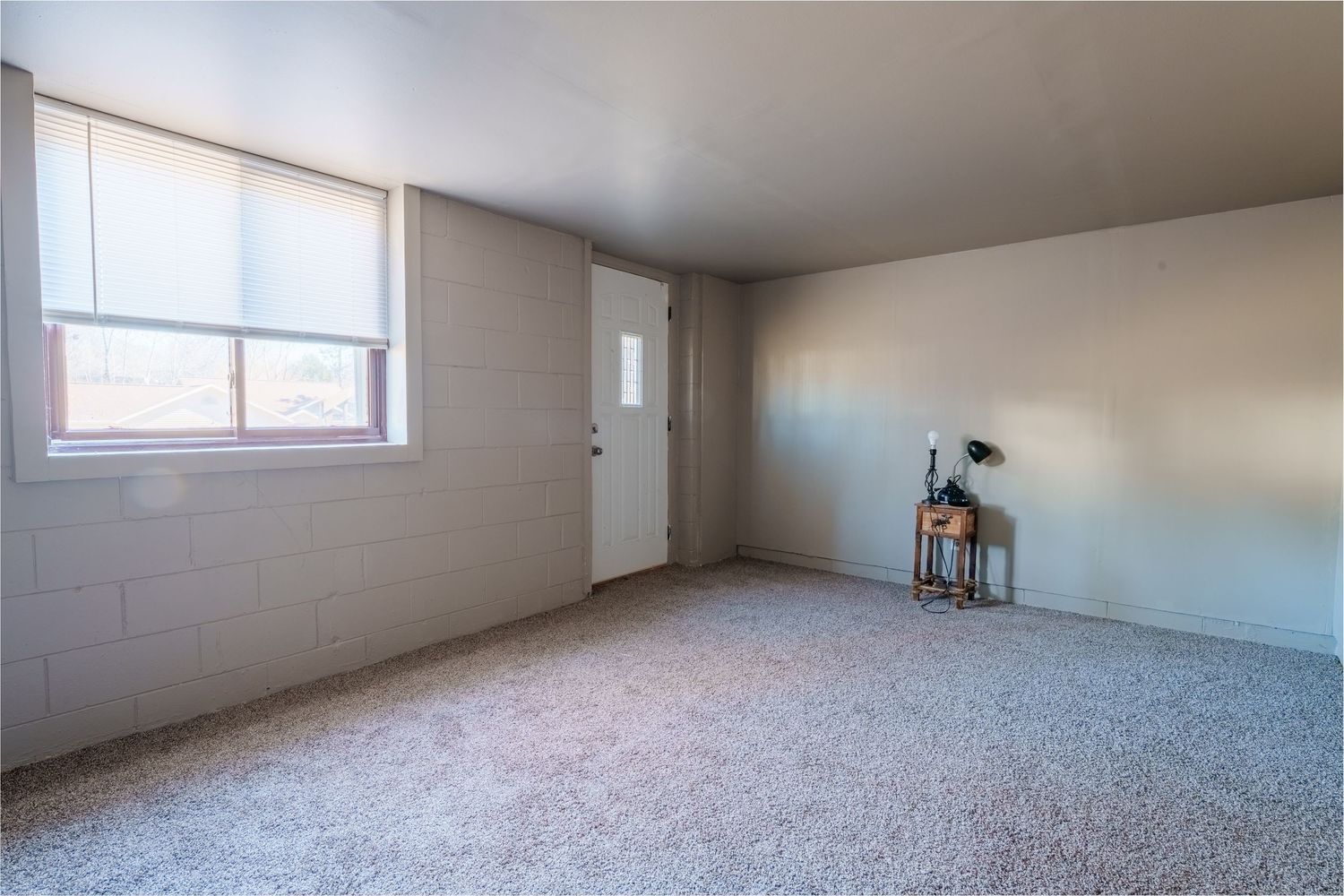 Empty room with beige carpet, white walls, and small window showing multiple angles of the unfurnished space.