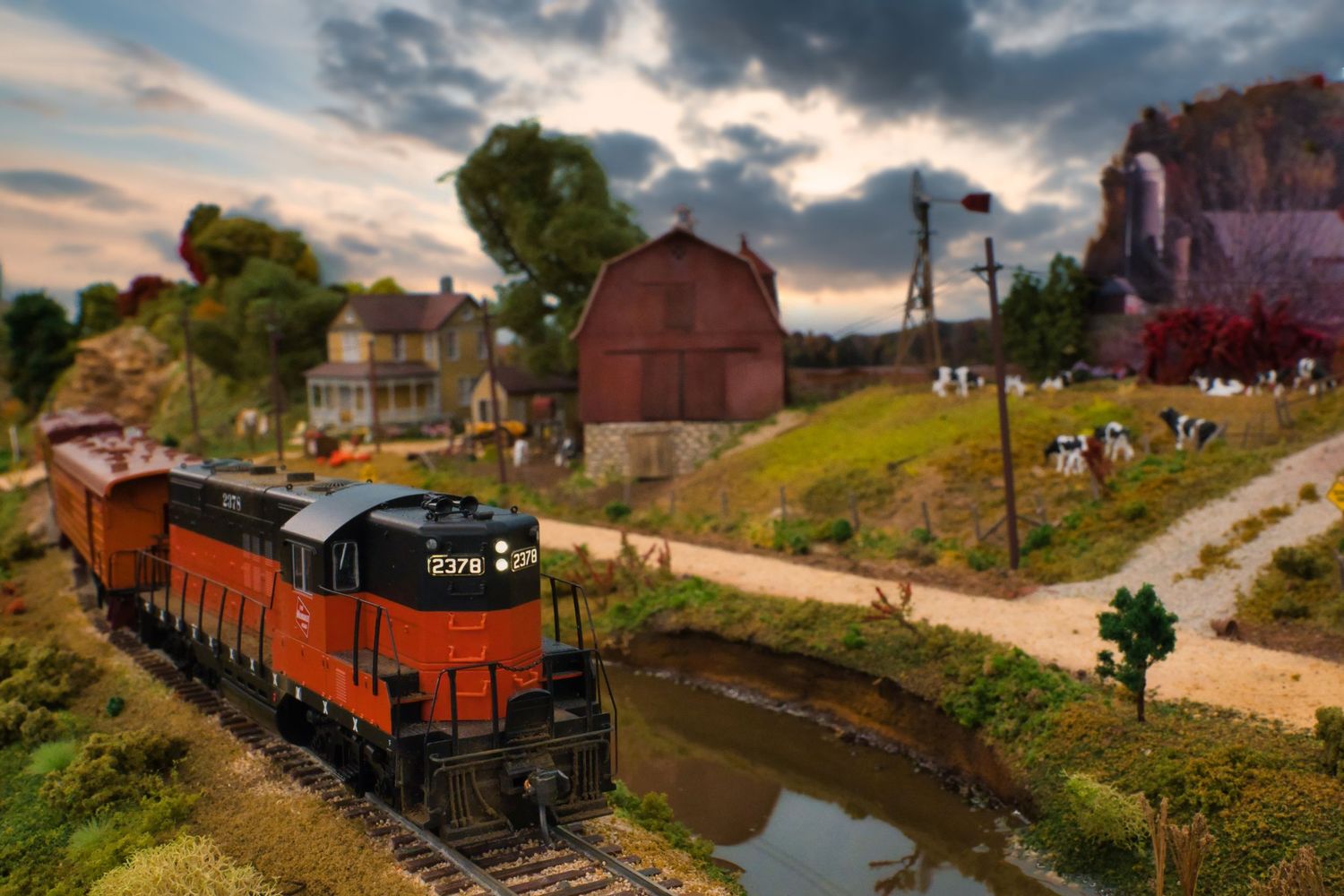 Scale model railroad scene shows freight cars and buildings along a curved track at sunset.