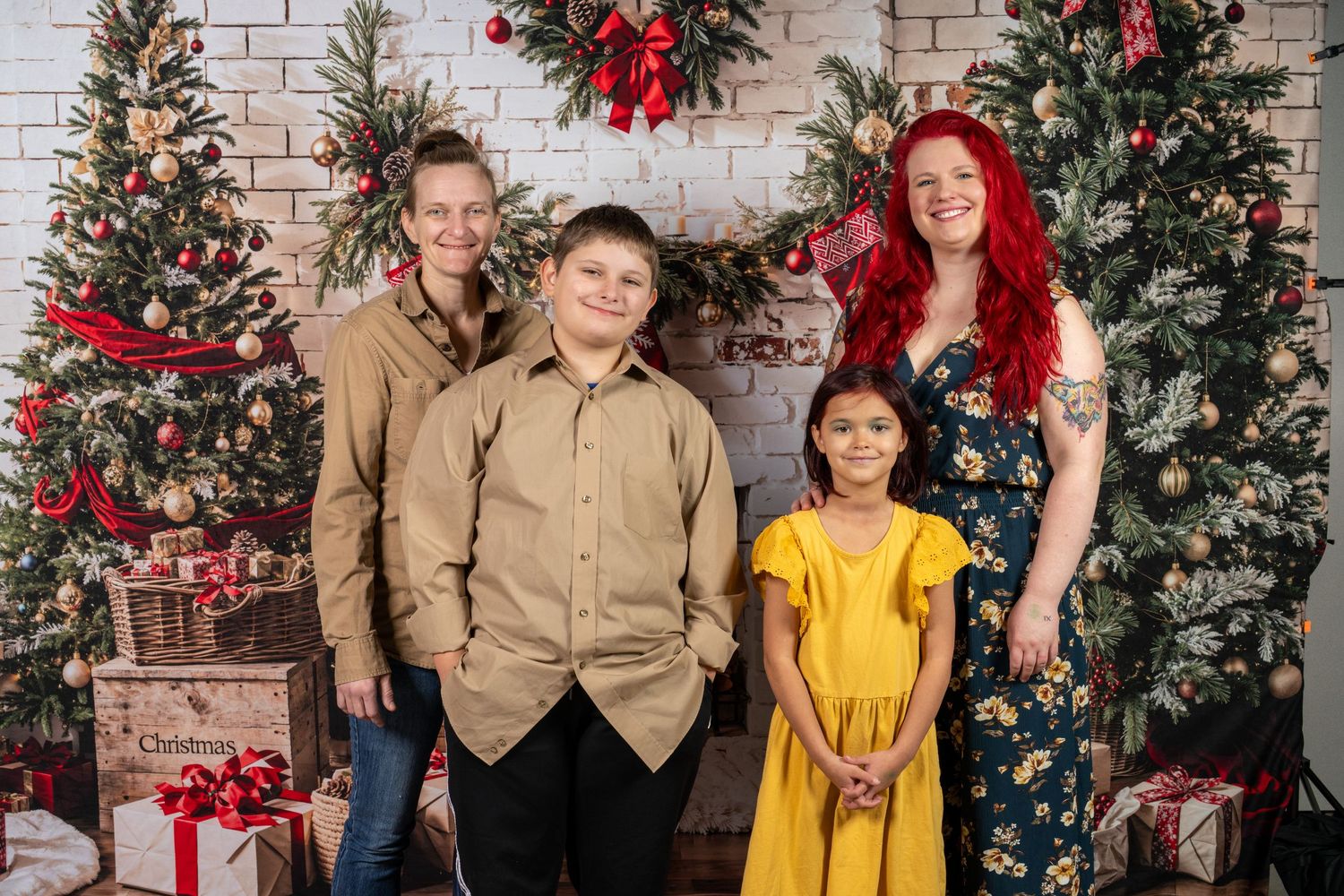 Family poses together in front of decorated Christmas trees and brick wall backdrop with festive holiday decor.