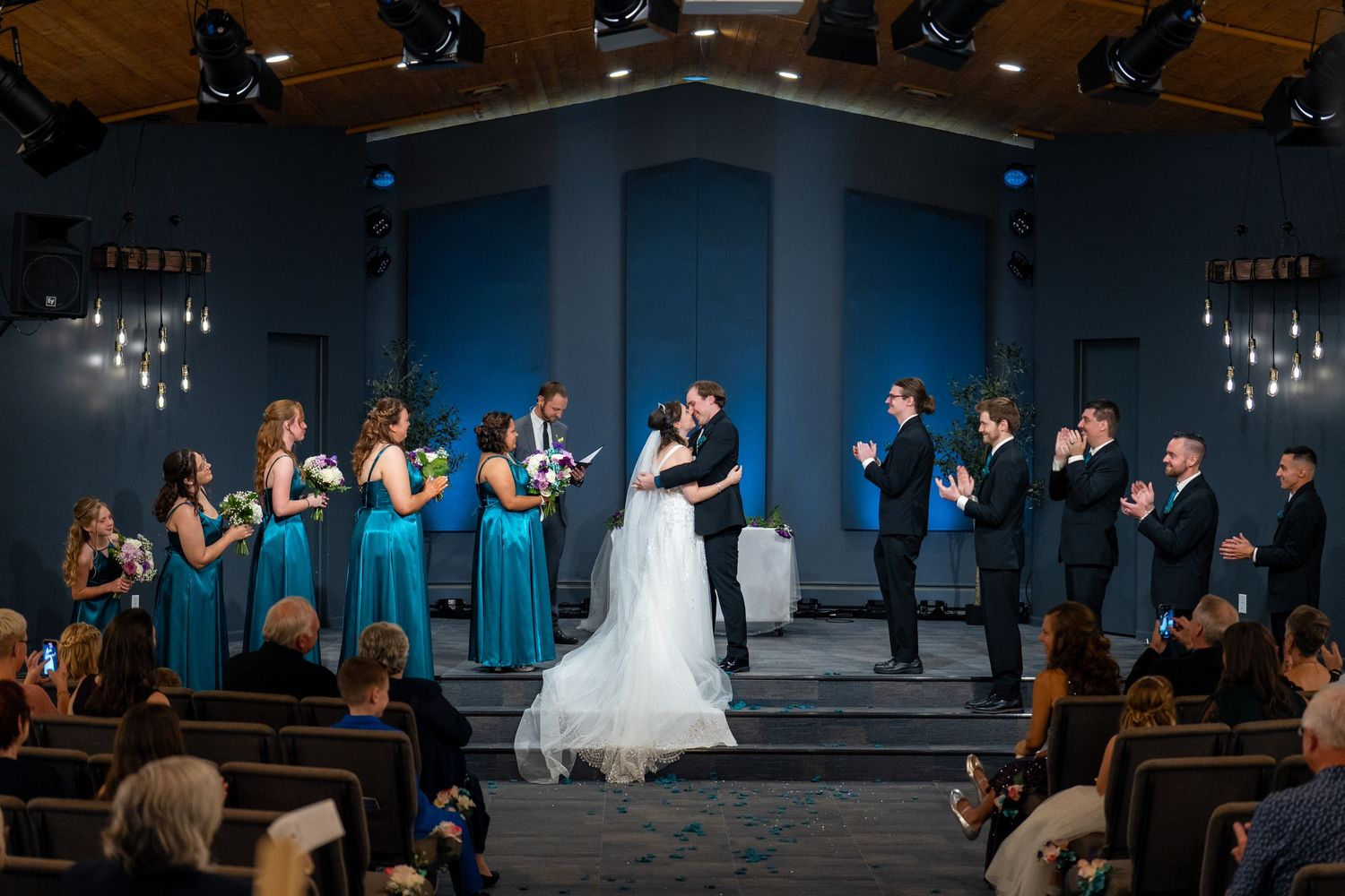 Wedding party performs synchronized dance routine in a dimly lit ballroom with blue uplighting and crystal chandeliers.