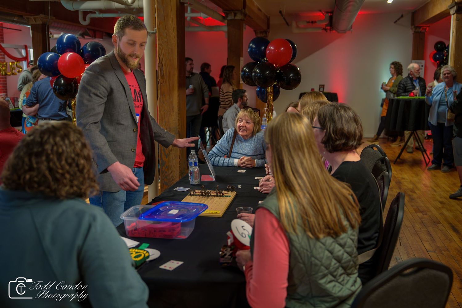 Guests socialize and interact at a festive indoor event with red and blue balloon decorations.