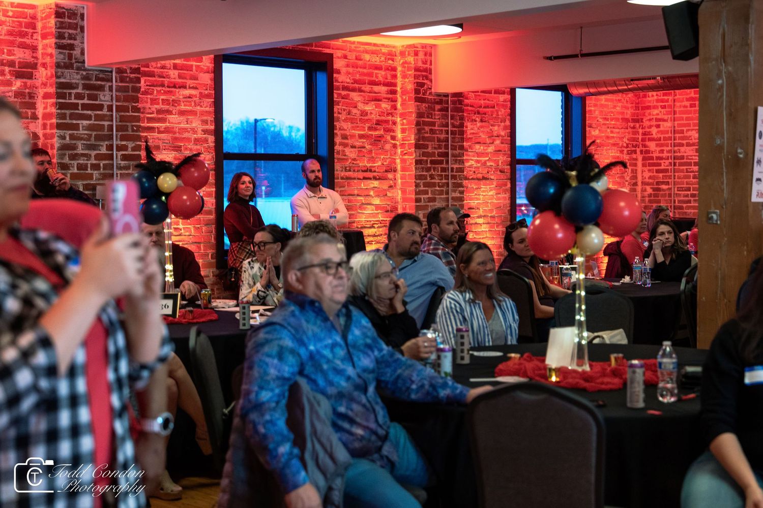 Guests enjoying a party event in a brick venue with red lighting, balloons, and festive decorations.