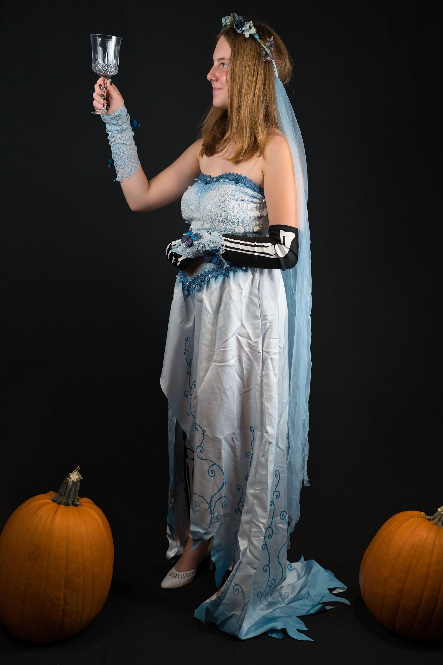 Halloween themed photo series with person in white dress posing next to orange pumpkins against black backdrop.