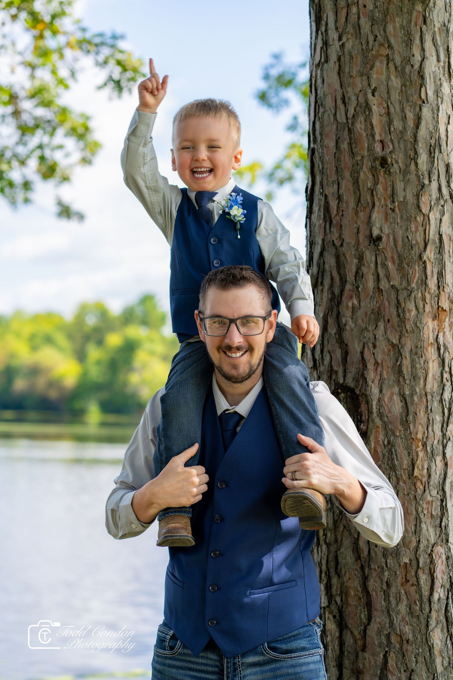 A playful outdoor family photoshoot by a lake with pine trees in the background shows joyful expressions and interactions.
