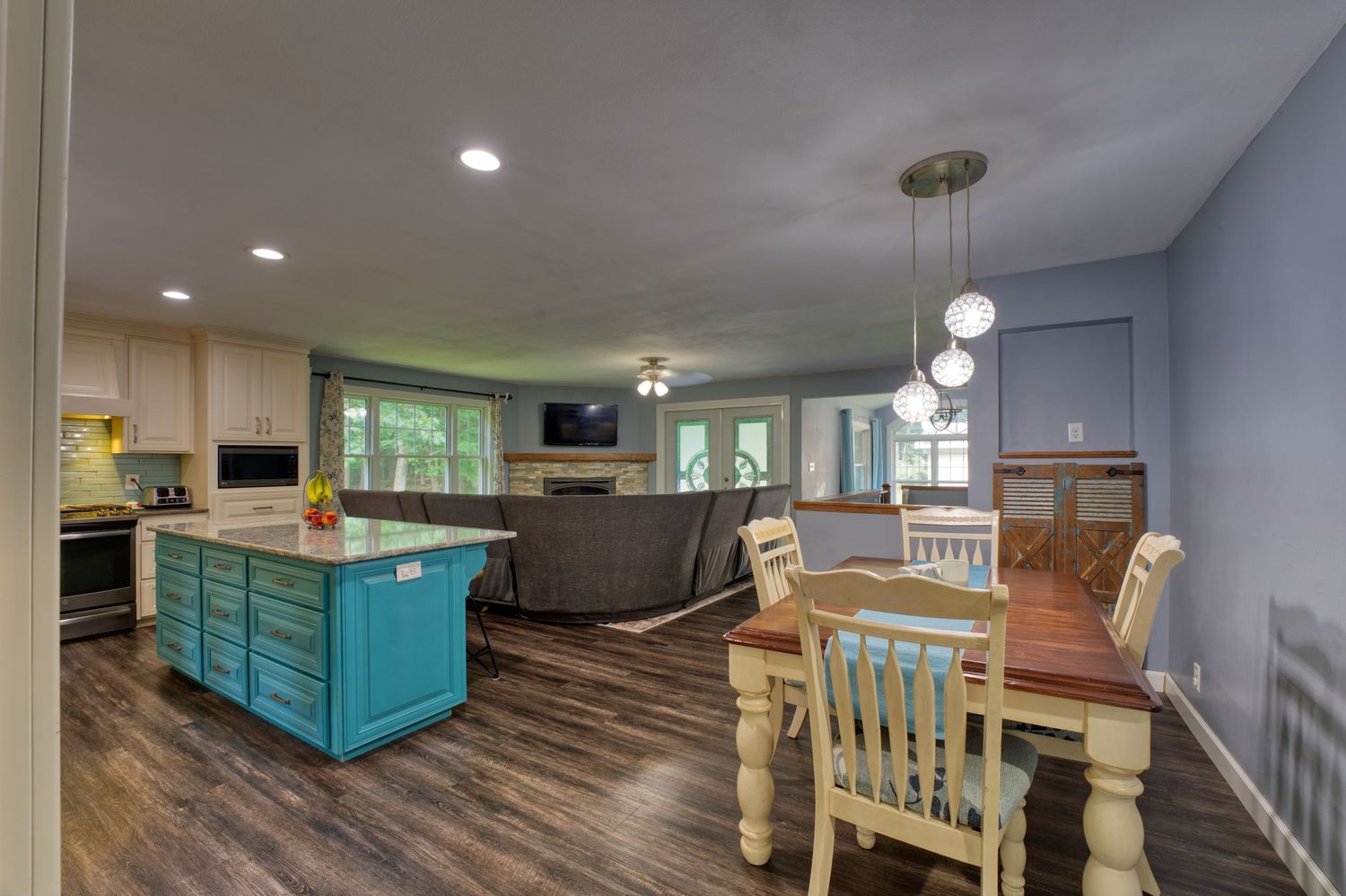 Open-concept kitchen with teal island, white cabinets, hardwood floors, and dining area with wooden table.