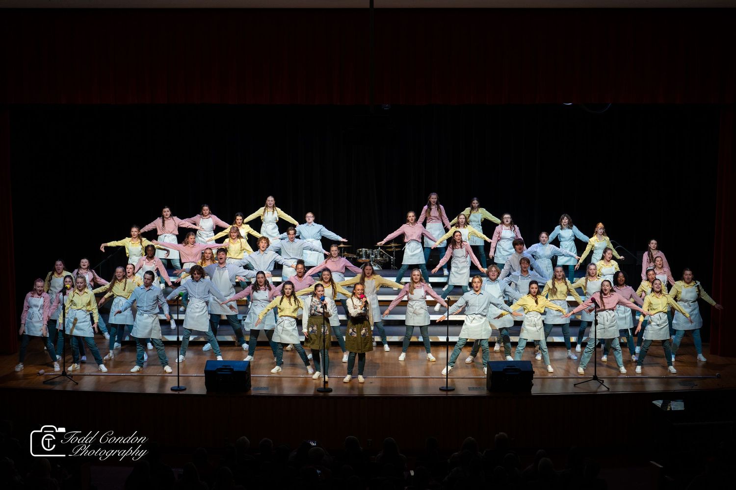Dance performers in colorful costumes create a synchronized formation on a dark stage during a theatrical show.
