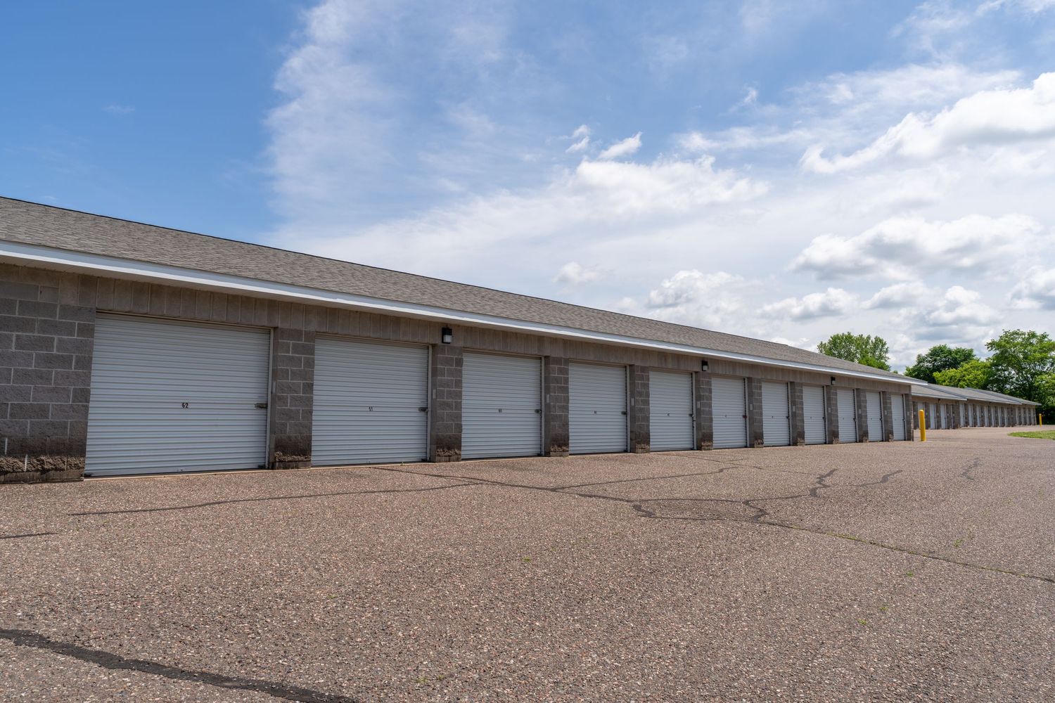 Row of storage units with brown gravel driveway under blue sky and white clouds.