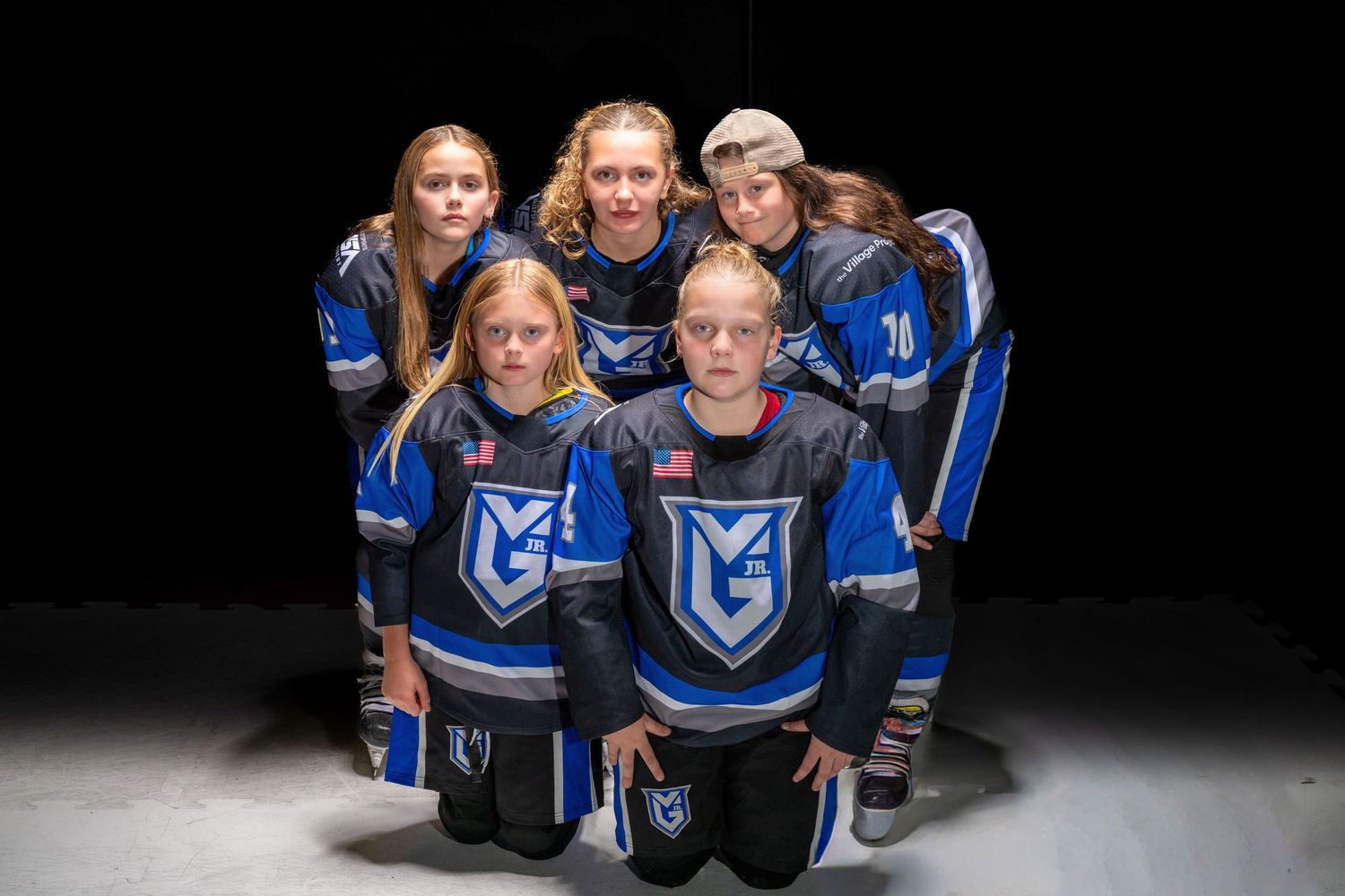 Athletes in blue and black uniforms pose together for a team photo shoot against a dark background.