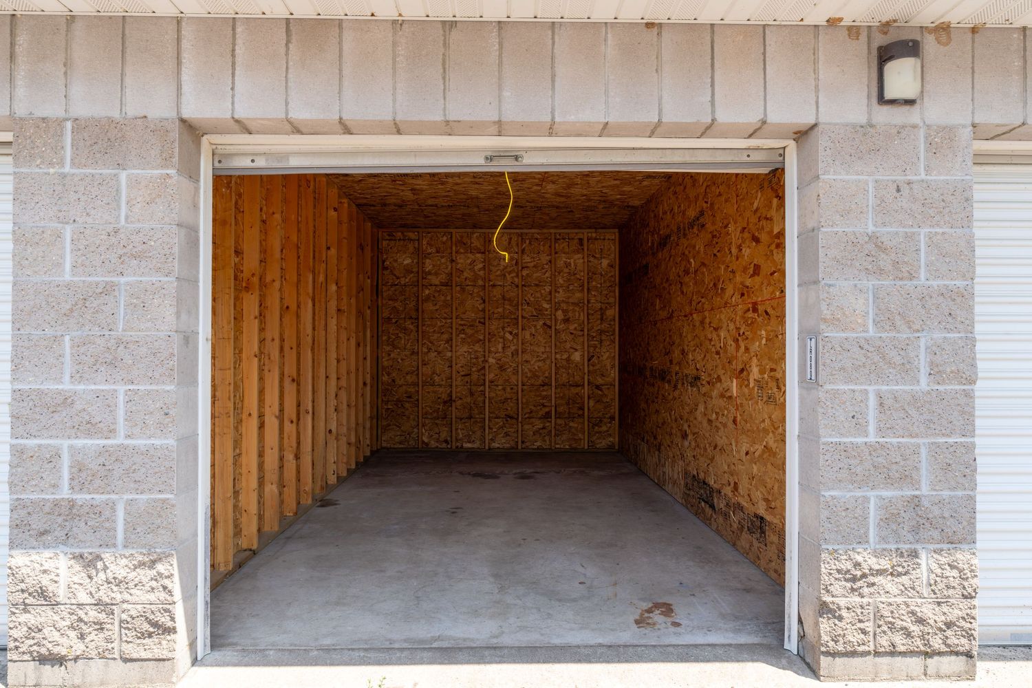 Empty storage unit with concrete floor, brick walls and oriented strand board interior panels shows available space.