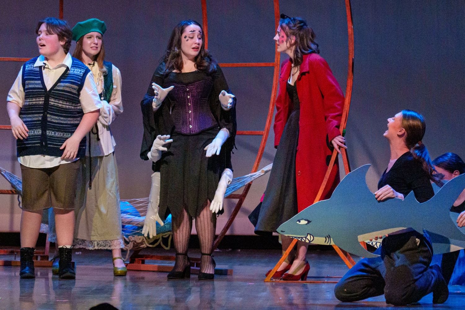 Theater performers in period costumes stand on stage during a musical production number.