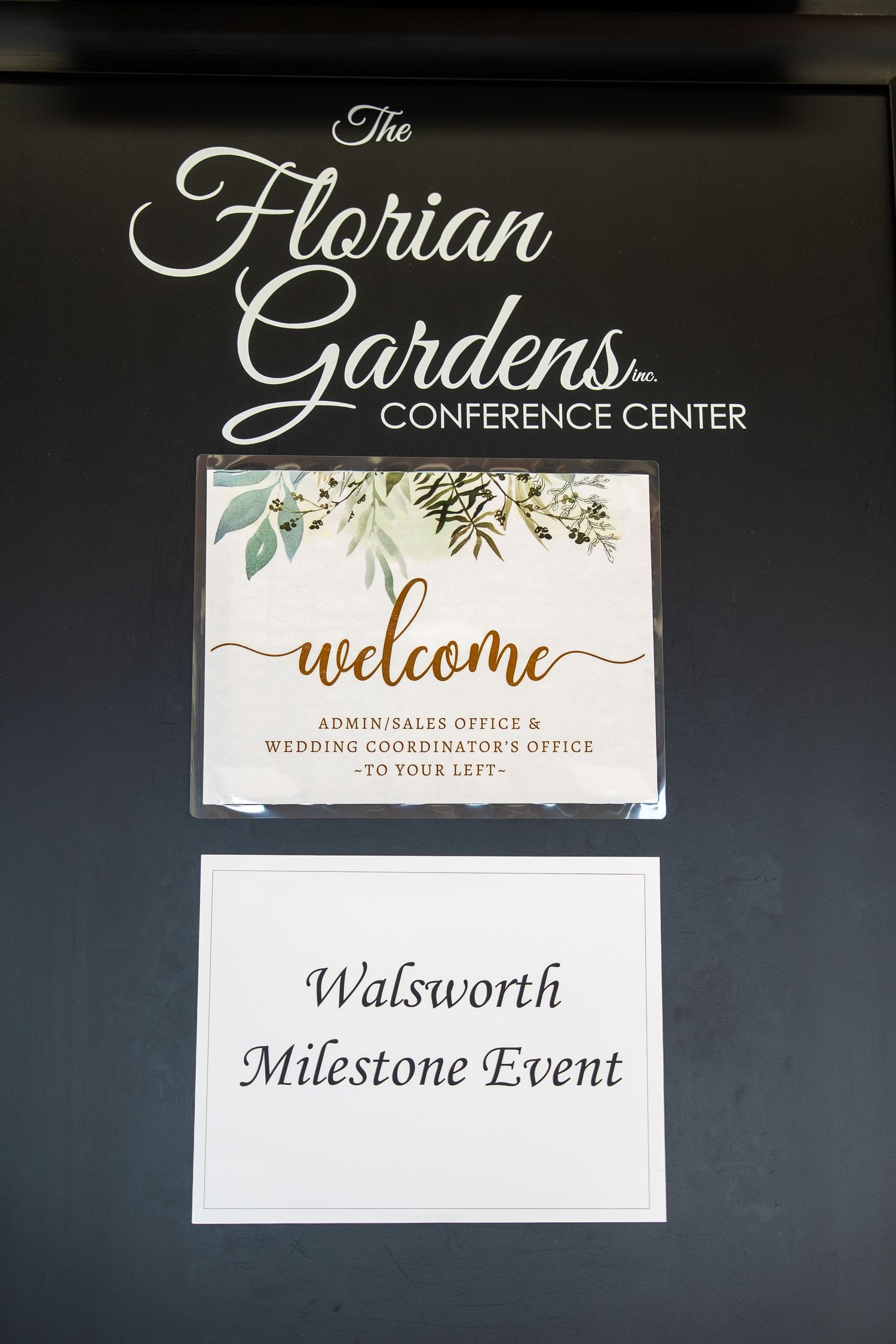 Elegant event venue signage displays welcome messages and directional text with floral accents on dark walls.