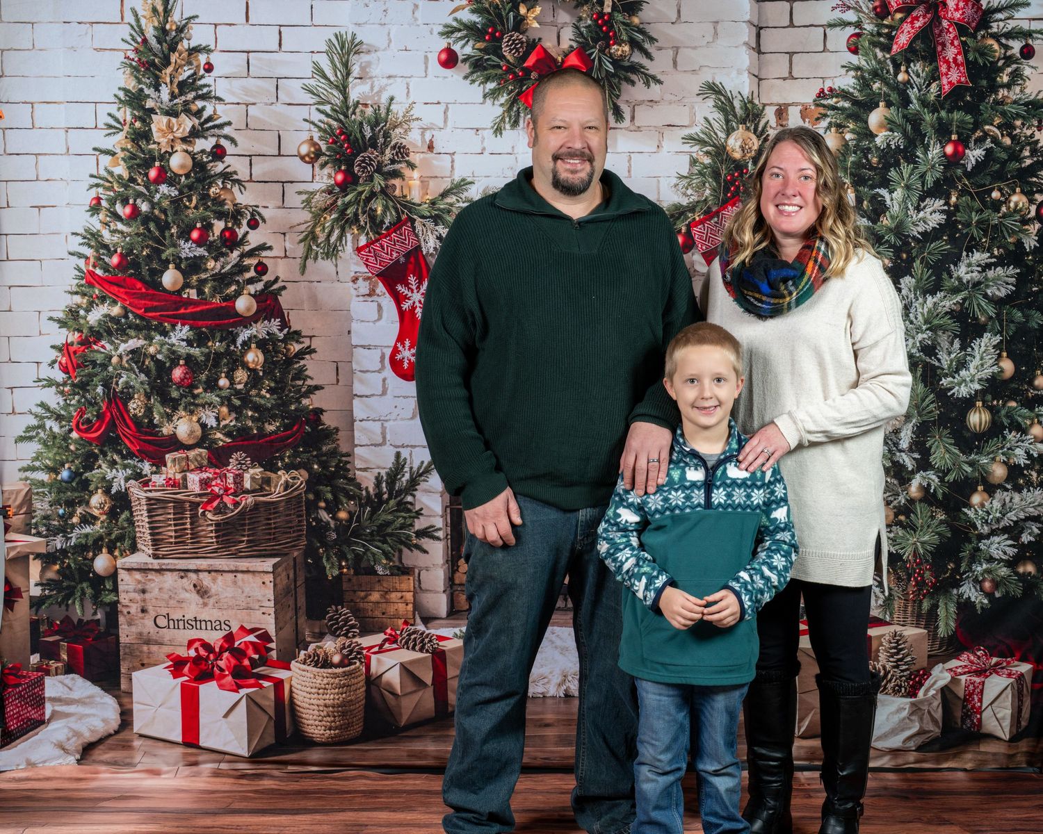 Decorated Christmas trees with red bows and wrapped presents create a festive holiday scene against a white brick wall.