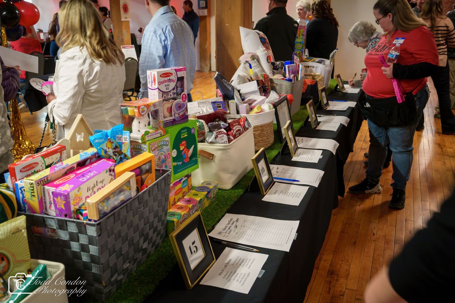 Silent auction tables displaying colorful gift baskets and bid sheets at a charity fundraiser event.
