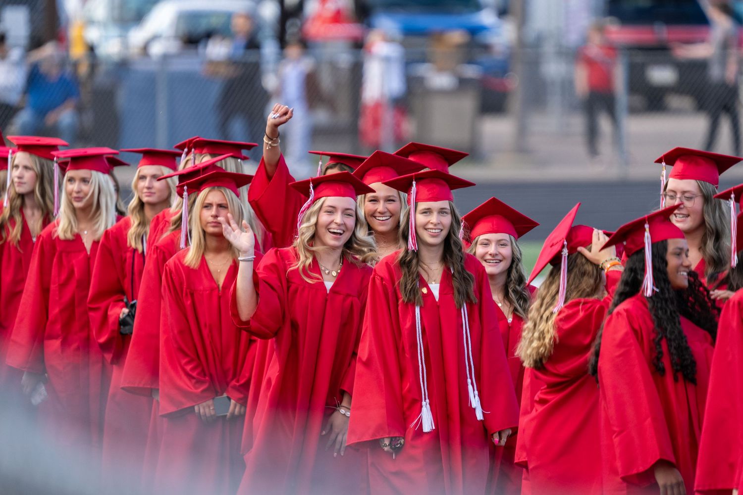 Group of female graduates in red caps and gowns smiling and celebrating at an outdoor graduation ceremony.