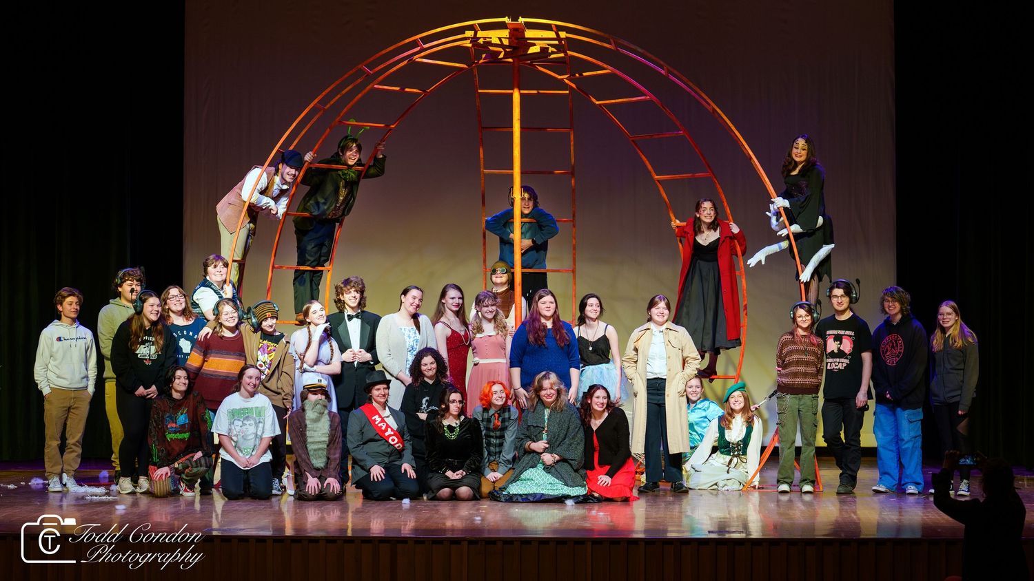 Theater performers stand on stage during a live musical performance with colorful stage lighting.