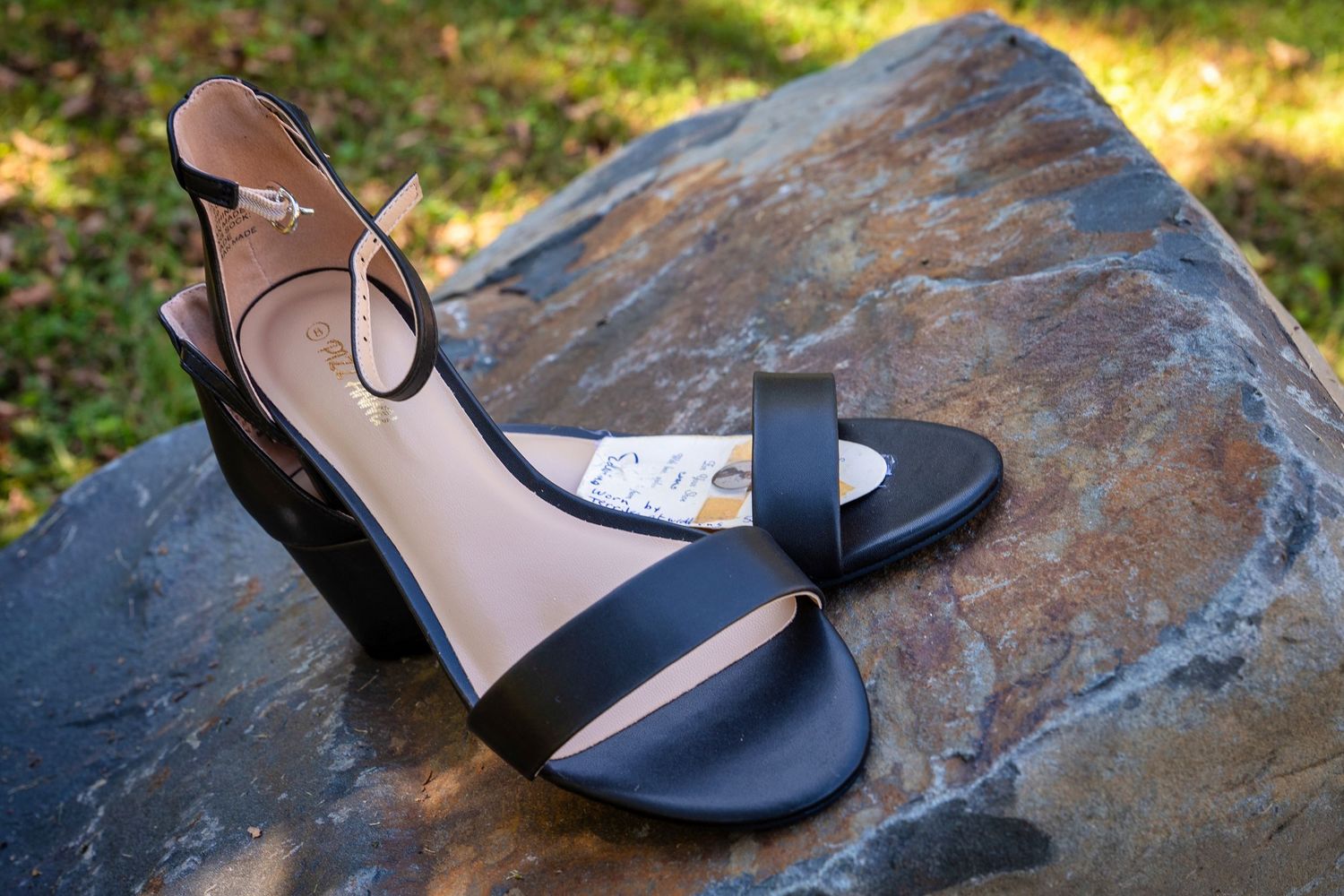 A series of black leather sandals displayed on a textured stone surface in natural outdoor lighting.