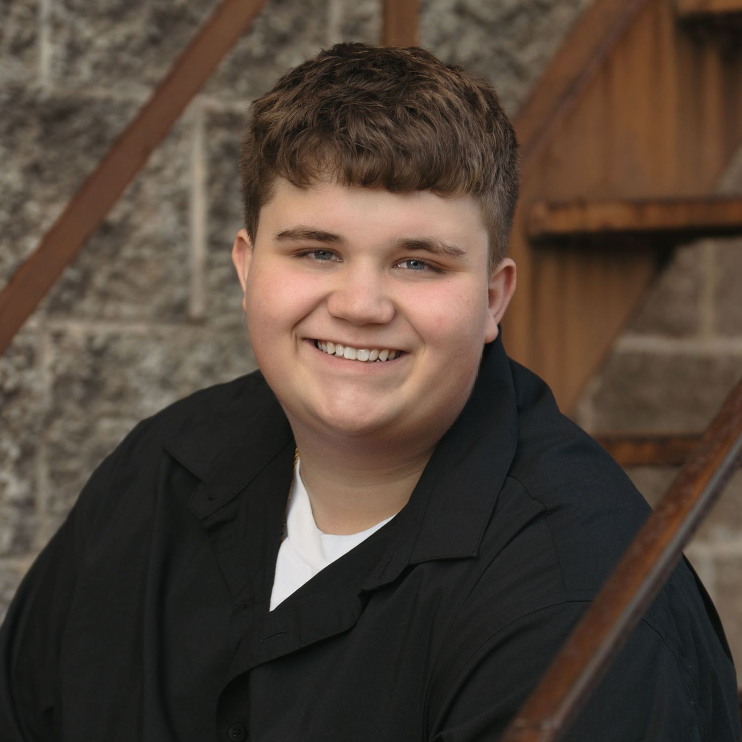 A student in a black suit jacket poses against a textured gray backdrop in a professional portrait series.