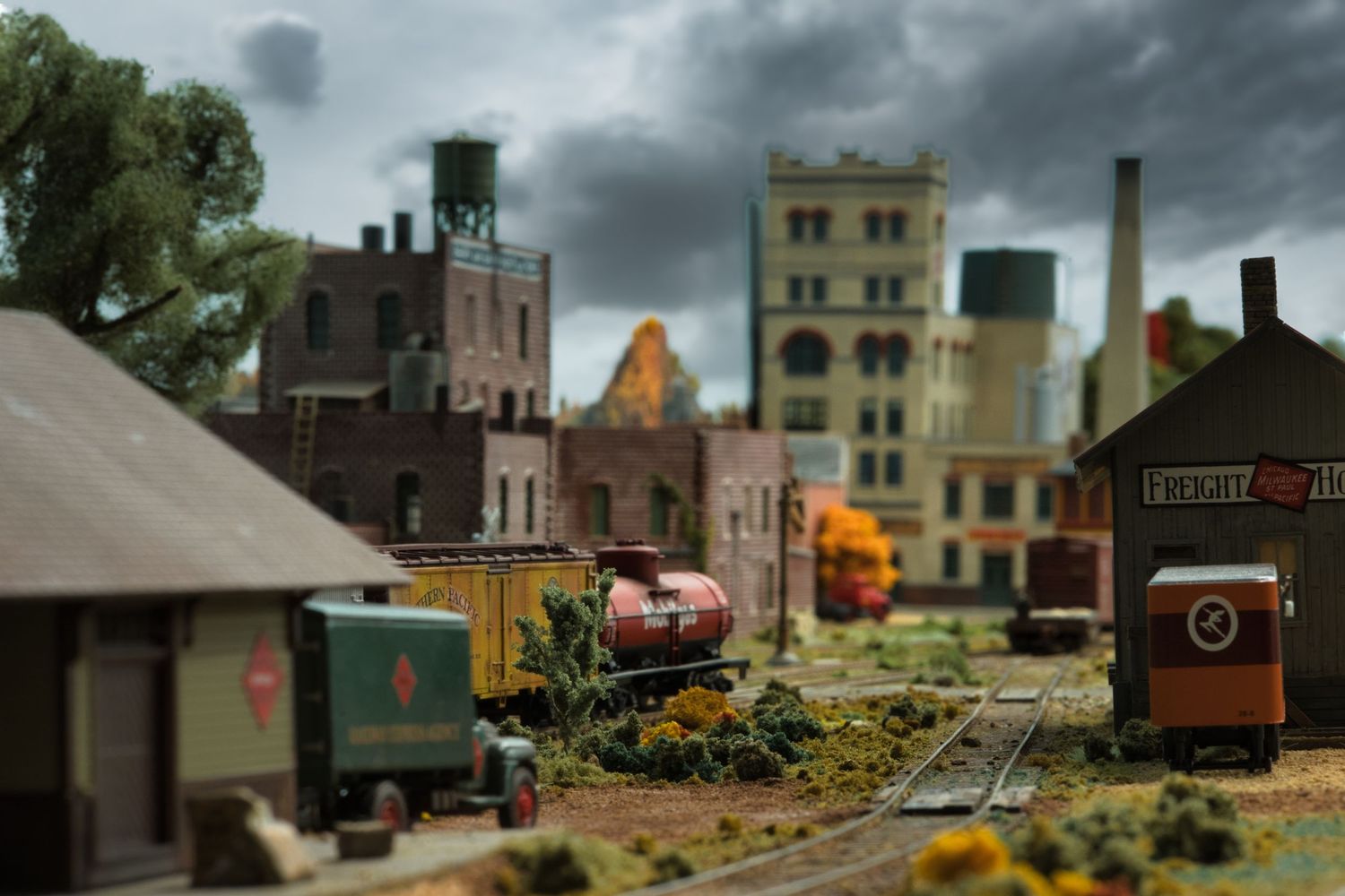 Model train layout features industrial buildings and scenery under dramatic stormy skies.