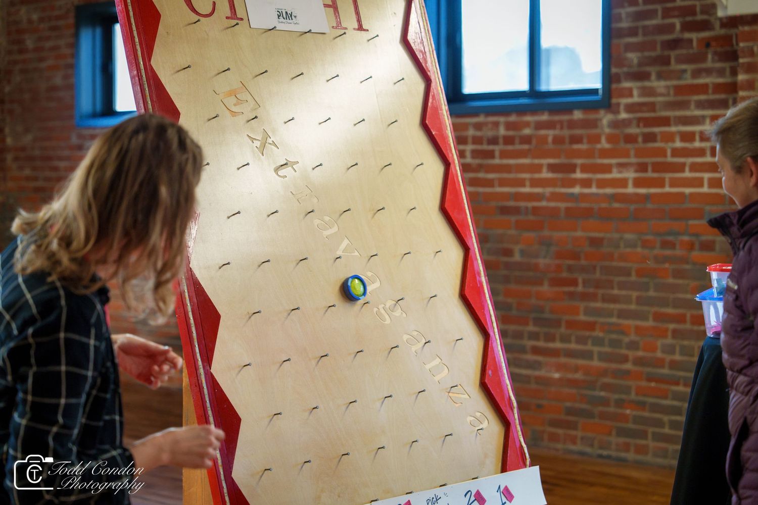People playing a plinko-style carnival game board with red and white decorative edges at an indoor event.