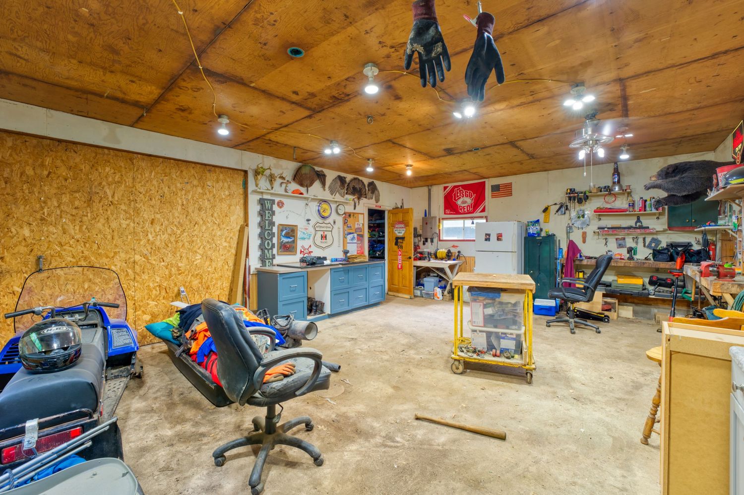 Spacious workshop with OSB walls, track lighting, office chairs, workbenches, and organized storage in a finished basement.