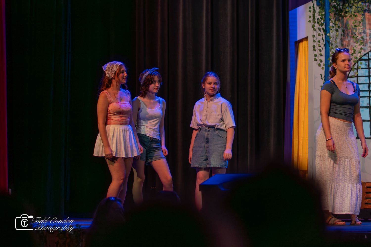 Performers on stage during a theatrical production with dramatic lighting and colorful costumes.