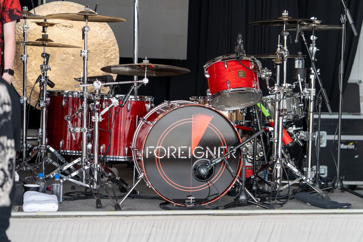 Multiple drum kits set up on stage with red and black colors visible in a concert performance setting.