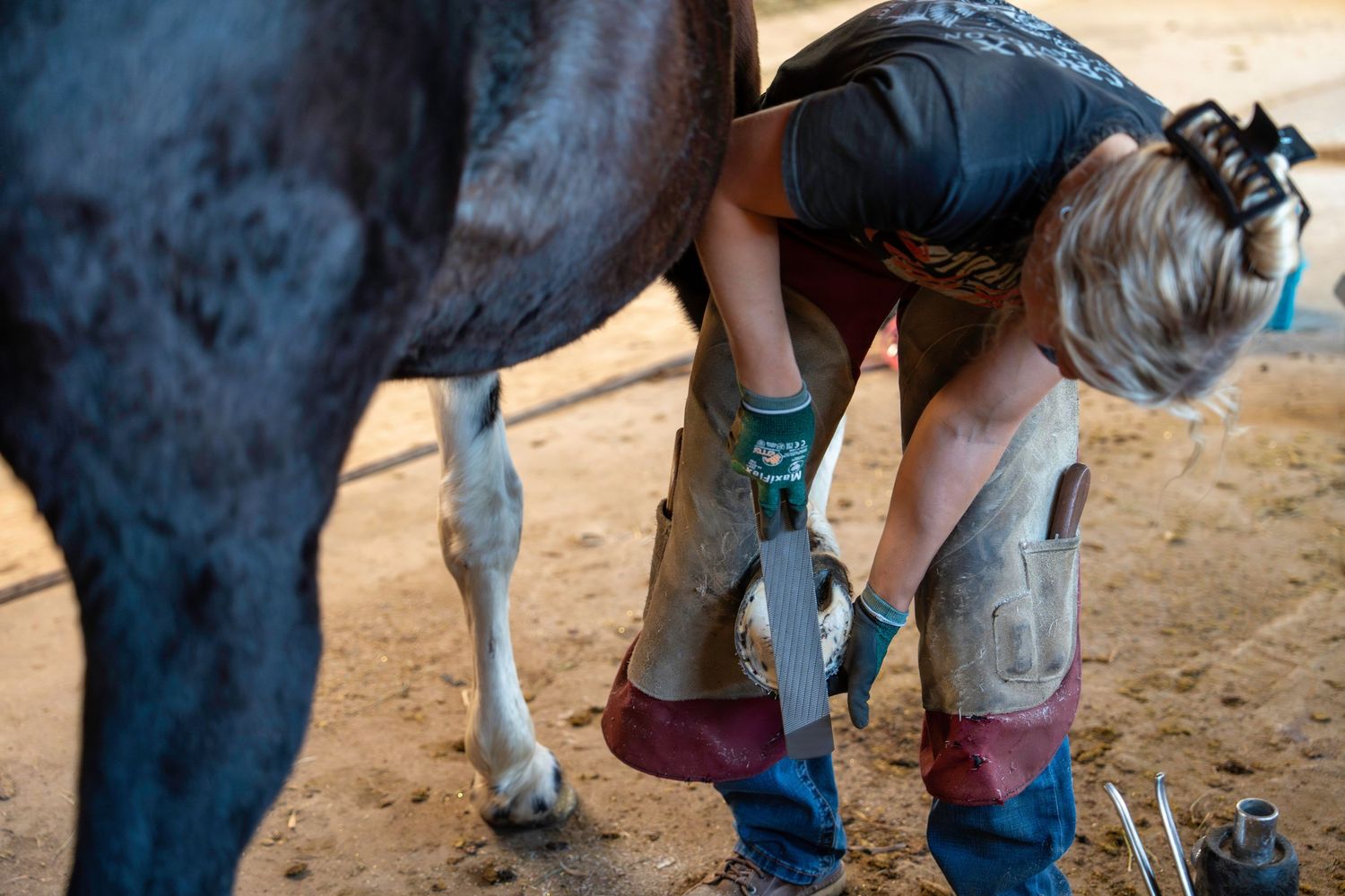 Close-up view of horse hooves and riding boots in a sandy arena.