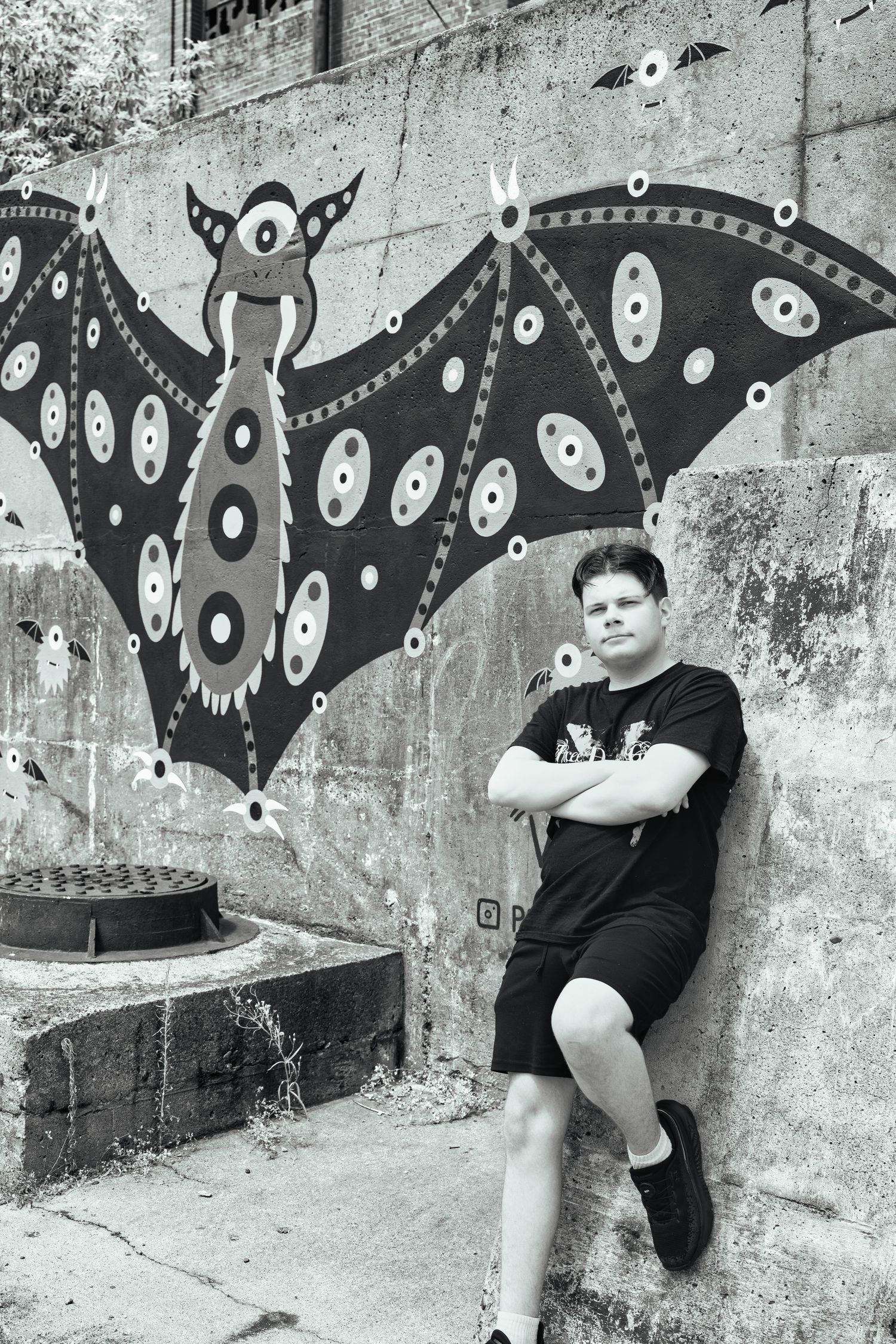 Black and white photo showing a decorative bat street art mural with circular patterns painted on a concrete wall.