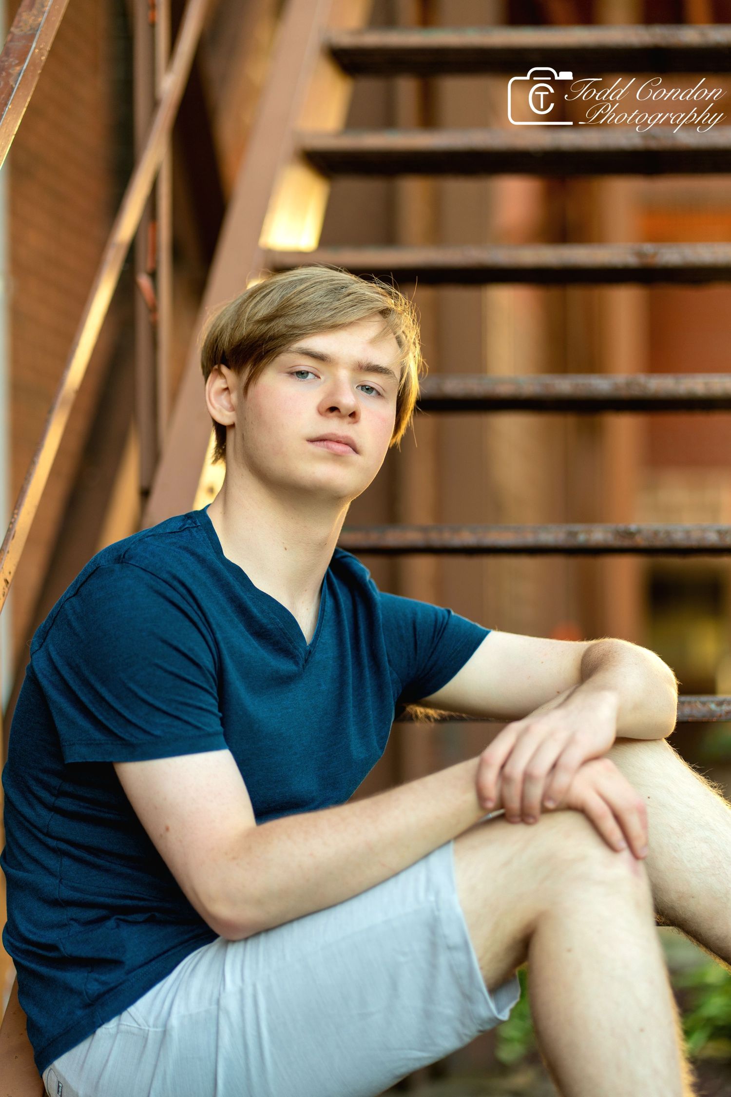 A person in a navy blue t-shirt sits casually outdoors against a blurred background in multiple poses.