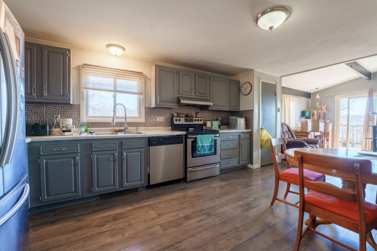 Modern kitchen with gray cabinets, stainless appliances, wood floors and dining area featuring large windows.