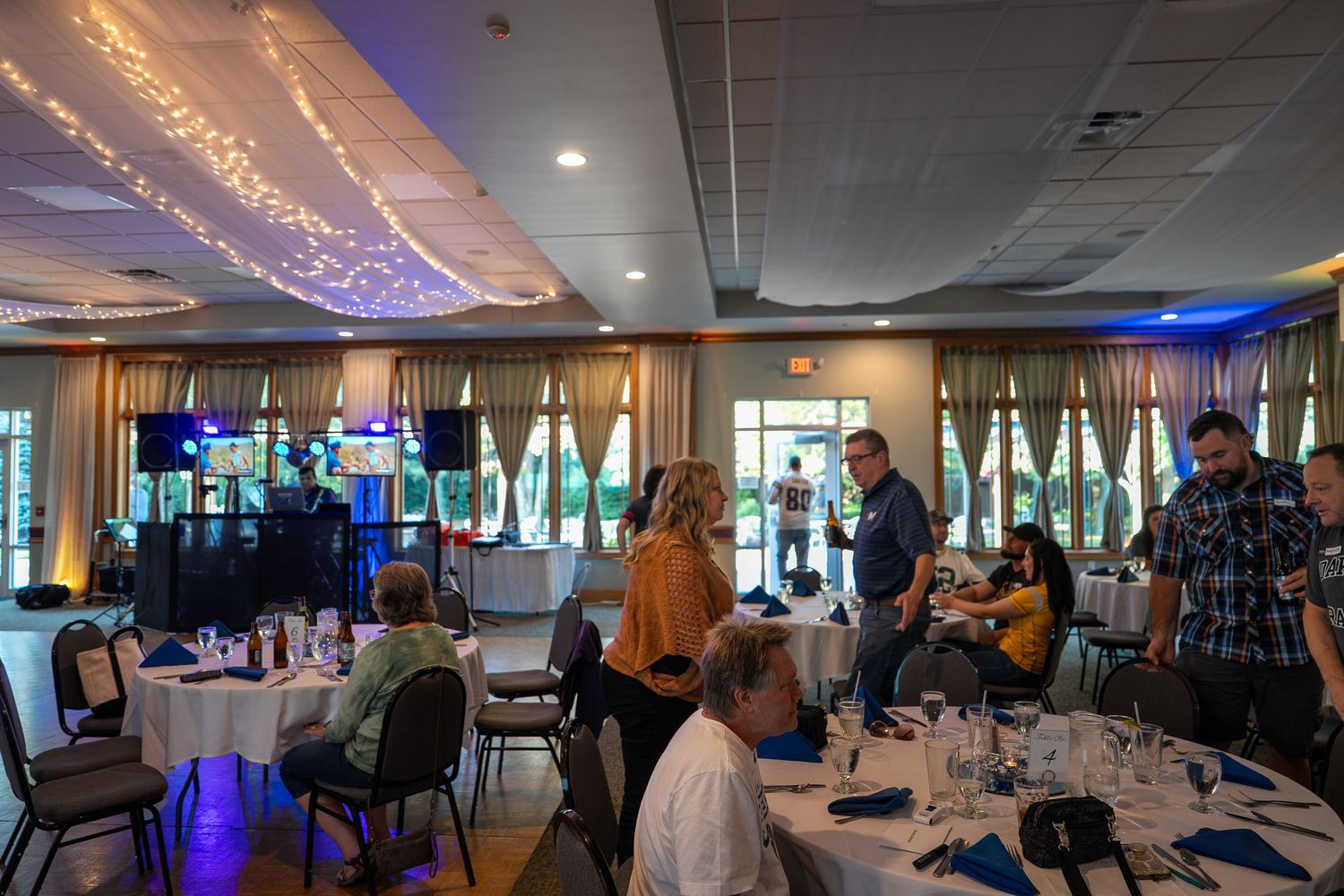 A panoramic view of a modern event space with string lights and blue ambient lighting illuminating tables and chairs.