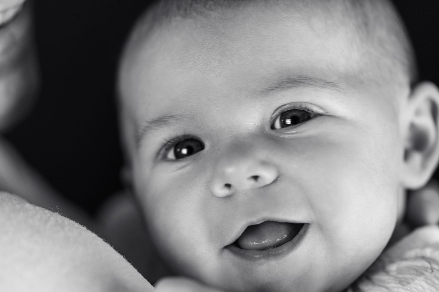 Close-up black and white portrait of a smiling newborn baby with bright eyes and chubby cheeks.