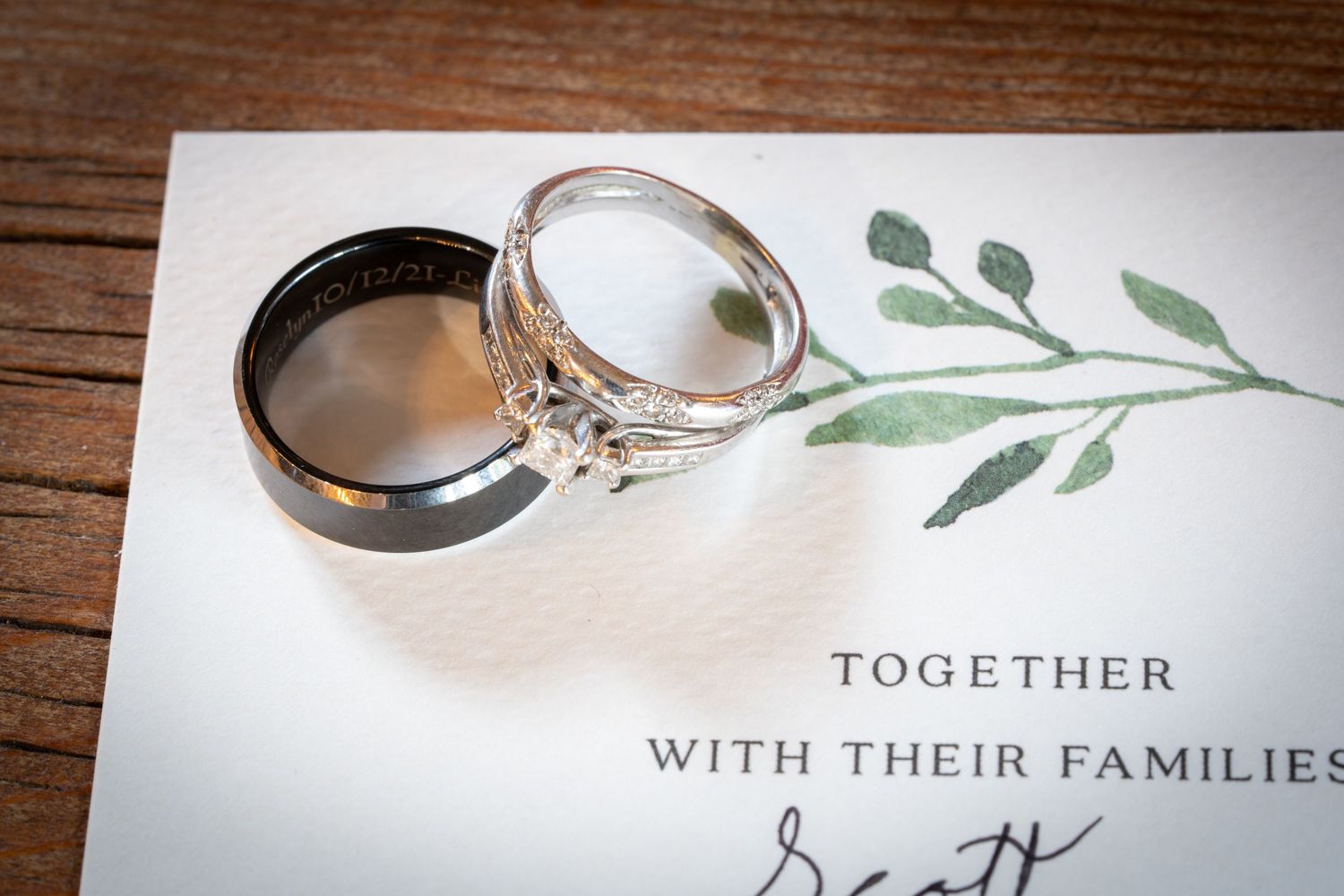 Wedding rings and invitation details photographed on a rustic wooden surface.