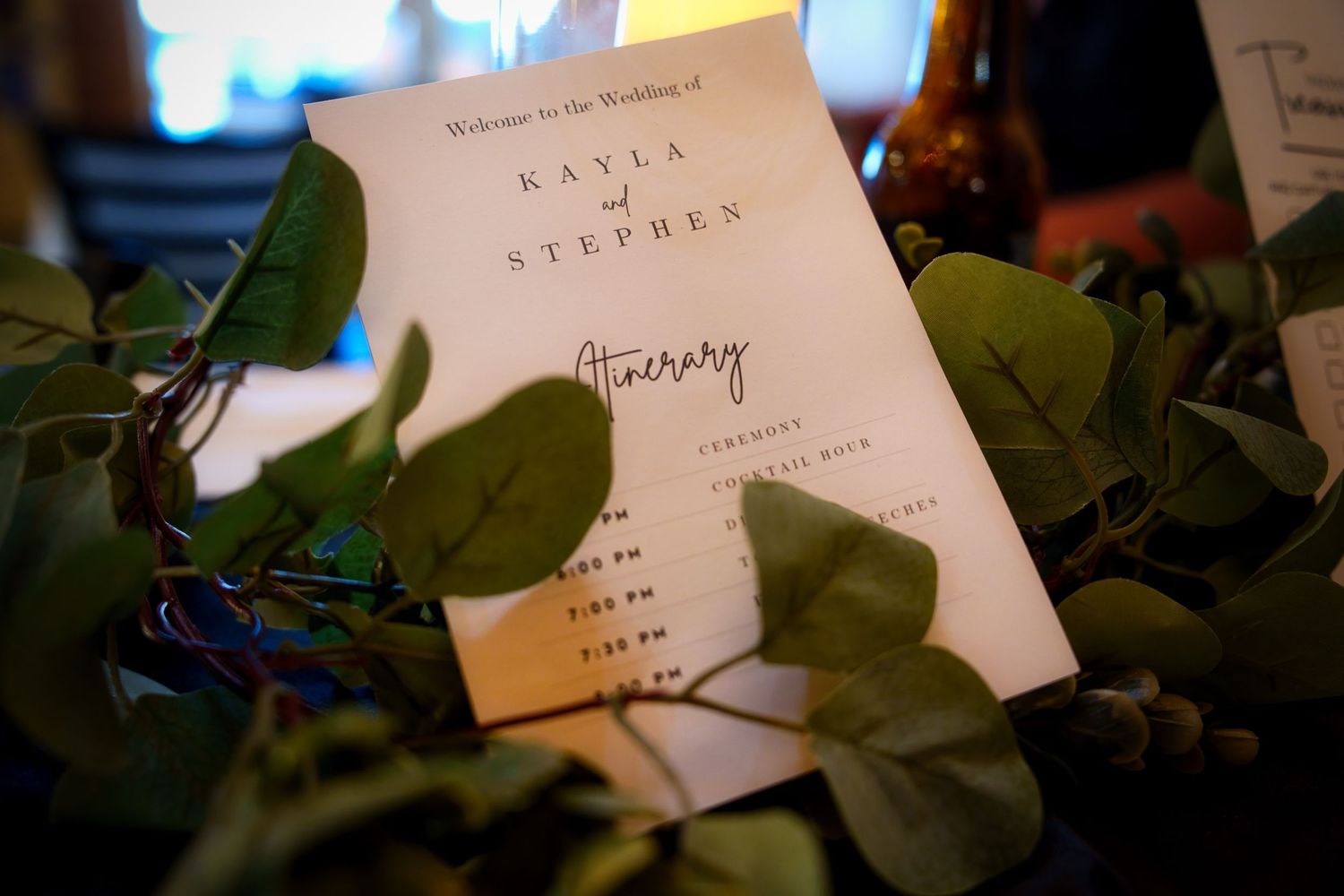 A book titled 'Kayla & Stephen' surrounded by green leaves and fairy lights in a dimly lit setting.