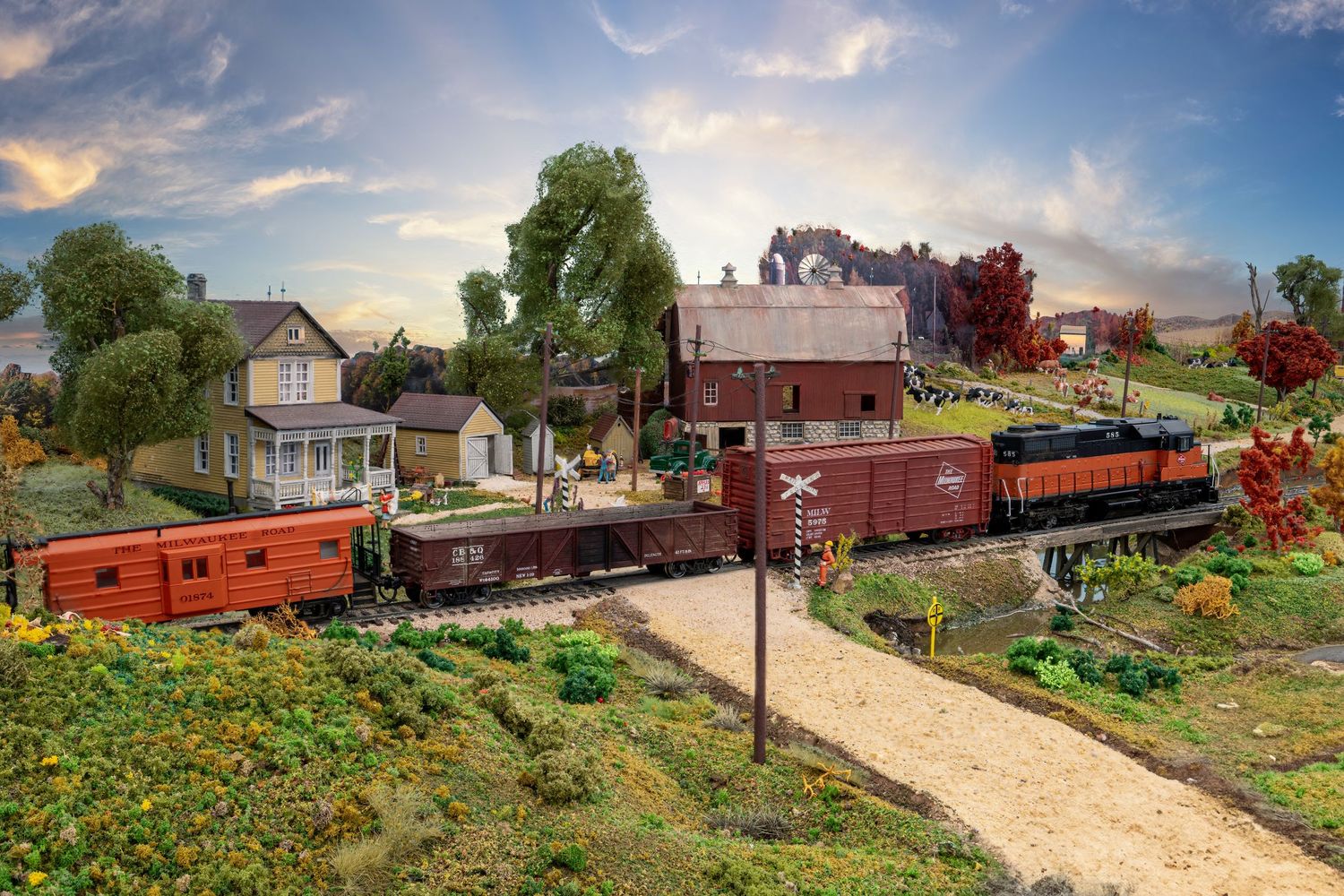 A model train set runs through a miniature village landscape with houses and colorful flowers along the track.