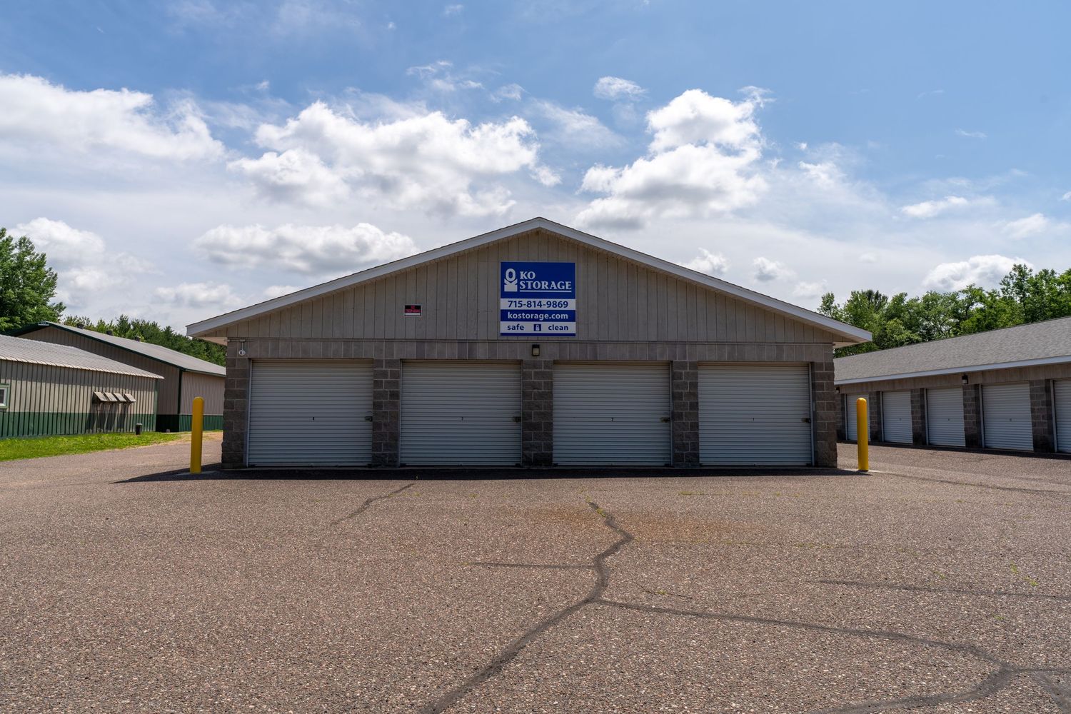 Multiple self storage units with beige exterior and roll-up doors under a blue sky.