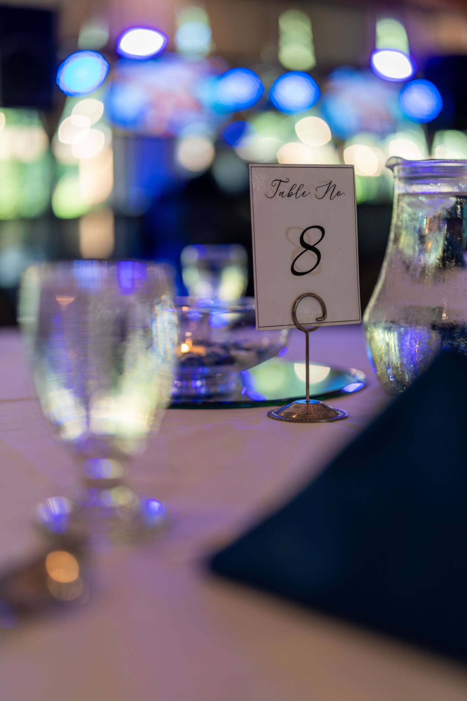 Table number cards with blurred bokeh lights create an elegant reception atmosphere at a formal event.